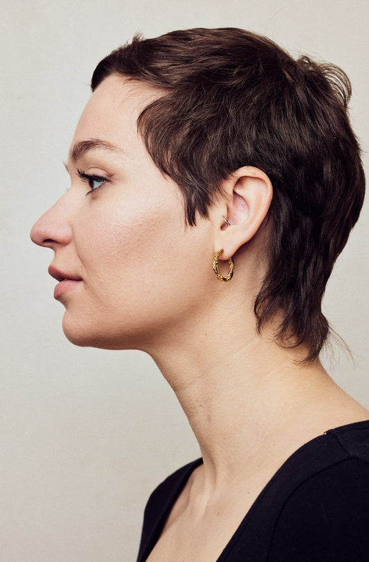 image of medium firework gold hoop earrings on model with short brown hair, headshot facing left