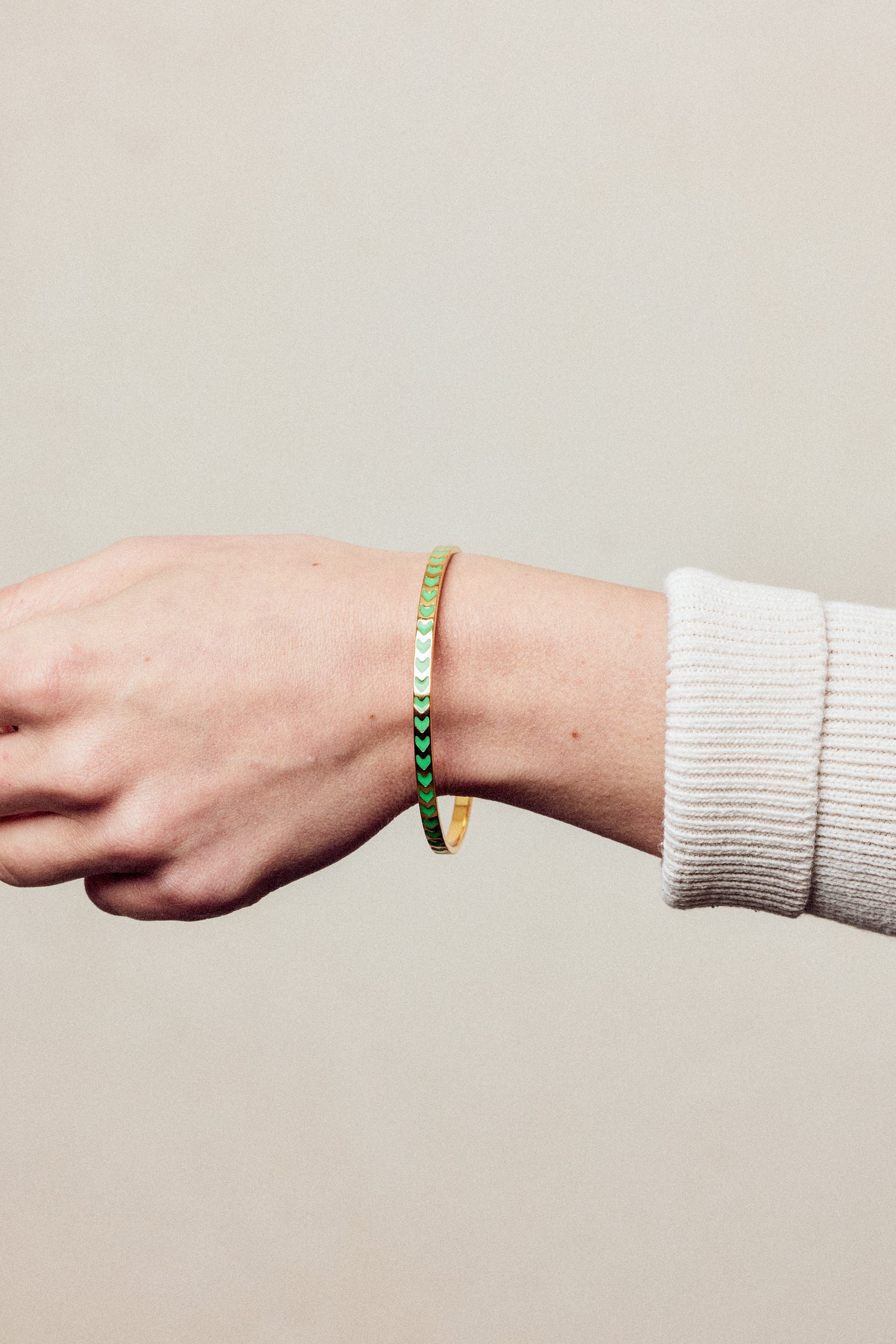 image of spark enamel bangle on wrist of woman with white skin wearing a cream ribbed top