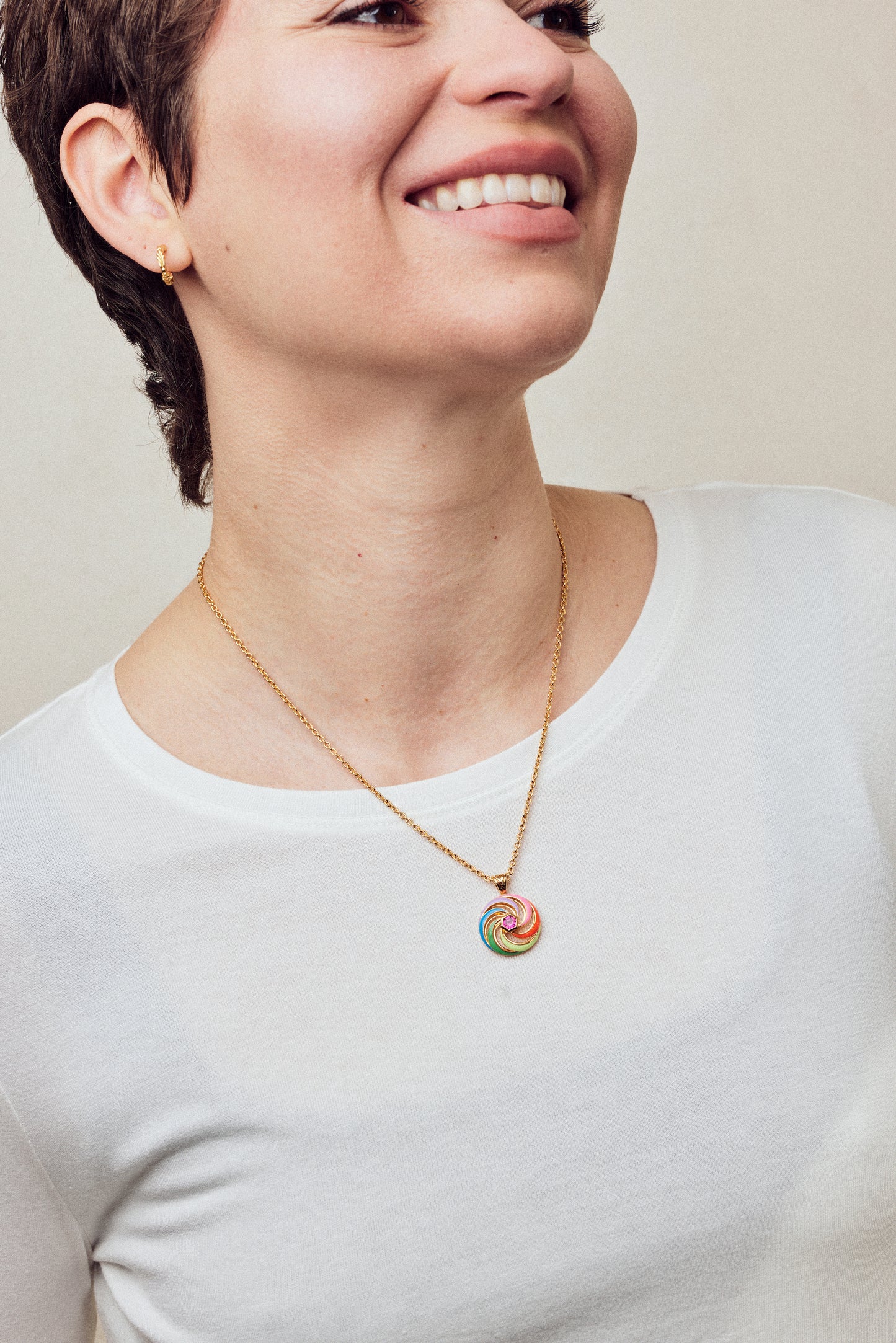 Image of enamel necklace with spinning disk on short chain on model in white top smiling