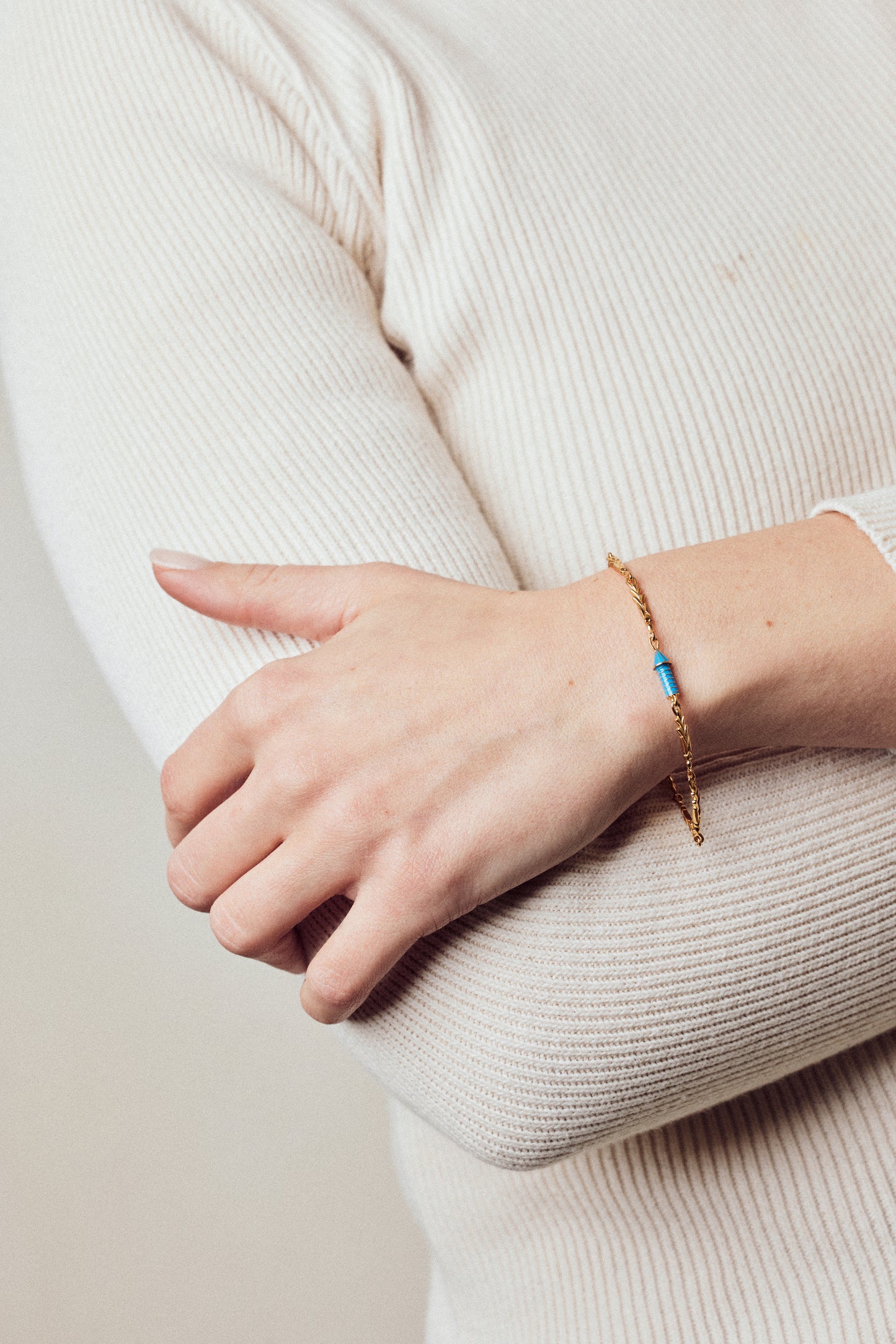 image of gold charm bracelet with blue enamel rocket on model in cream ribbed top with hand holding arm
