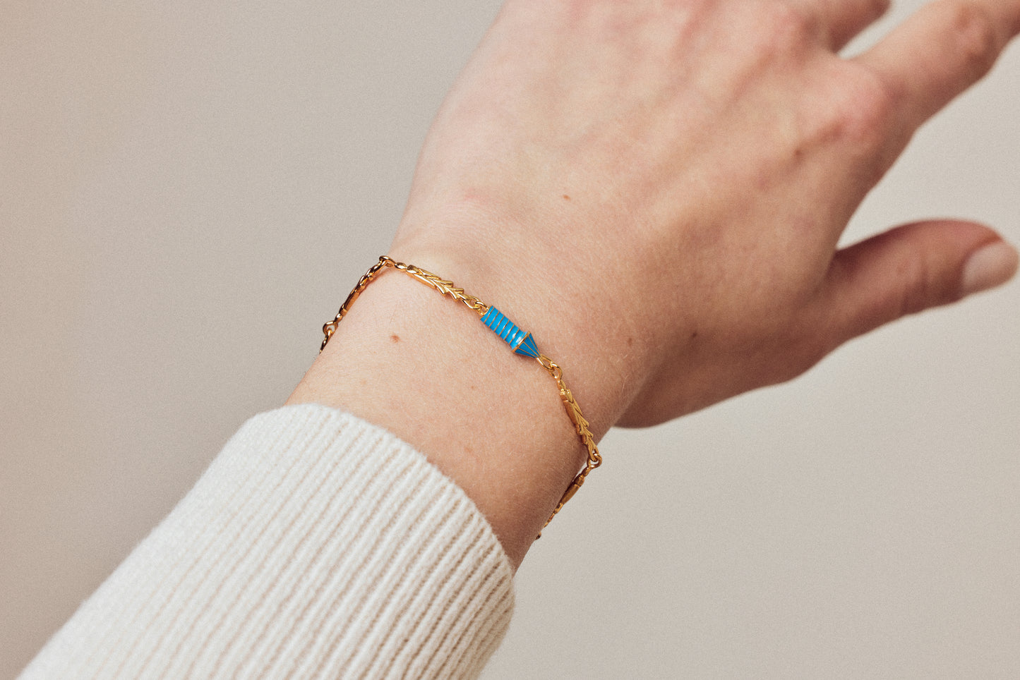 image of gold charm bracelet with blue enamel rocket on wrist with outstretched hand