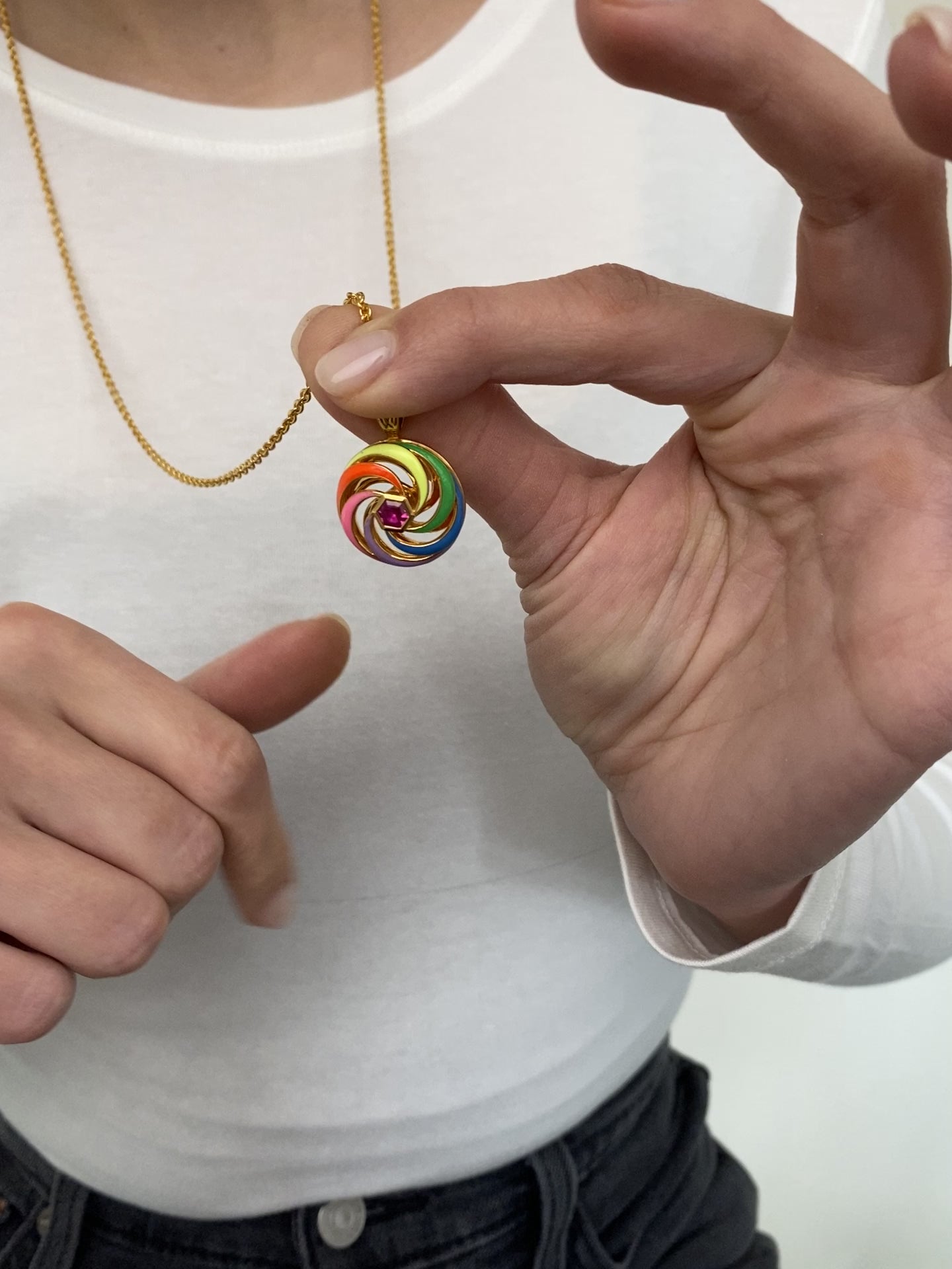 video of spinning disk enamel necklace in multi-colour enamel with close up on hands of model spinning it