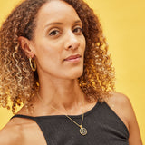 image of diamond sparkler initial necklace, letter A on short chain, on model with curly brown hair and brown skin against yellow background