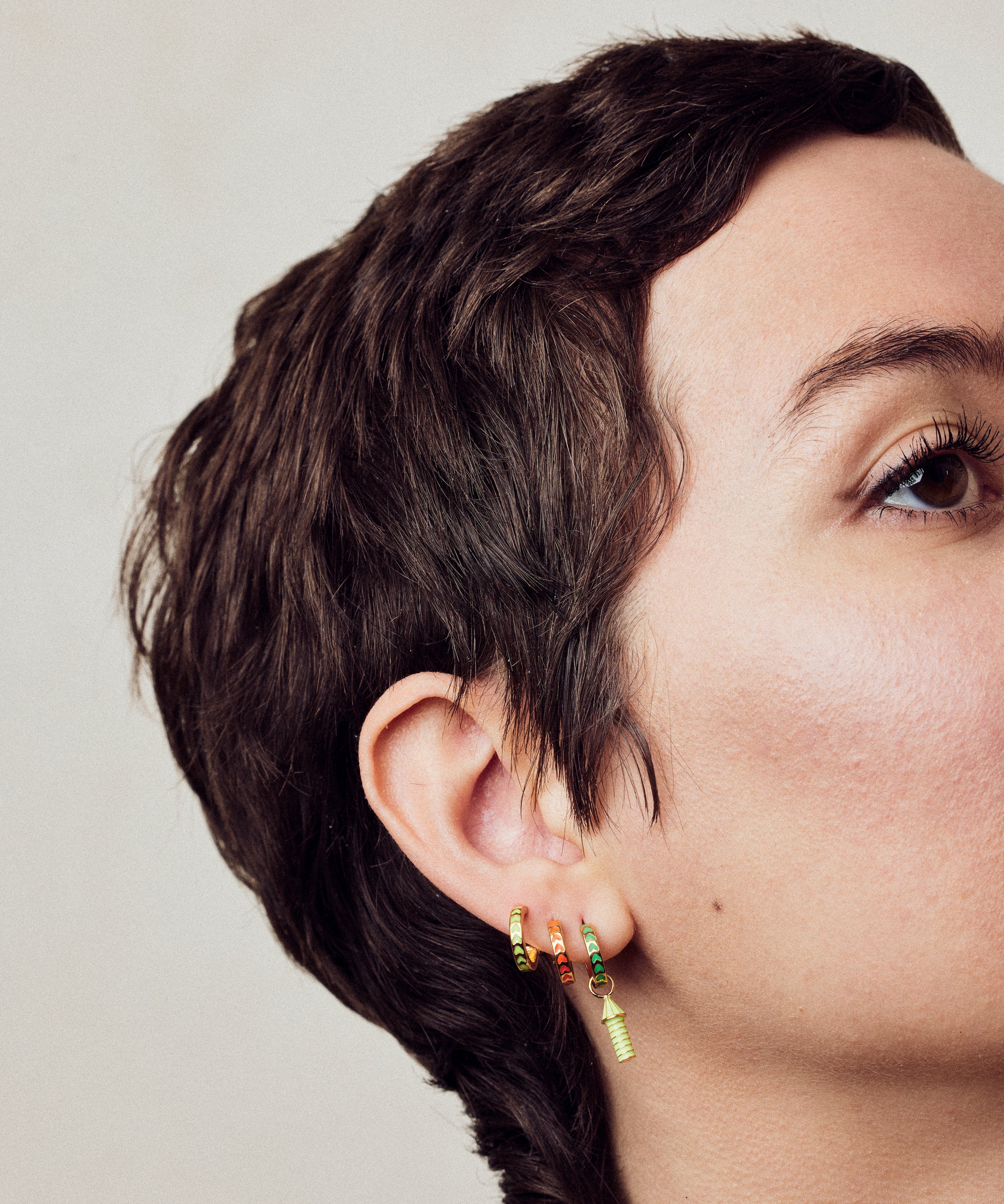 image of spark hoop enamel earrings stacked on ear with rocket enamel earrings on model with short brown hair