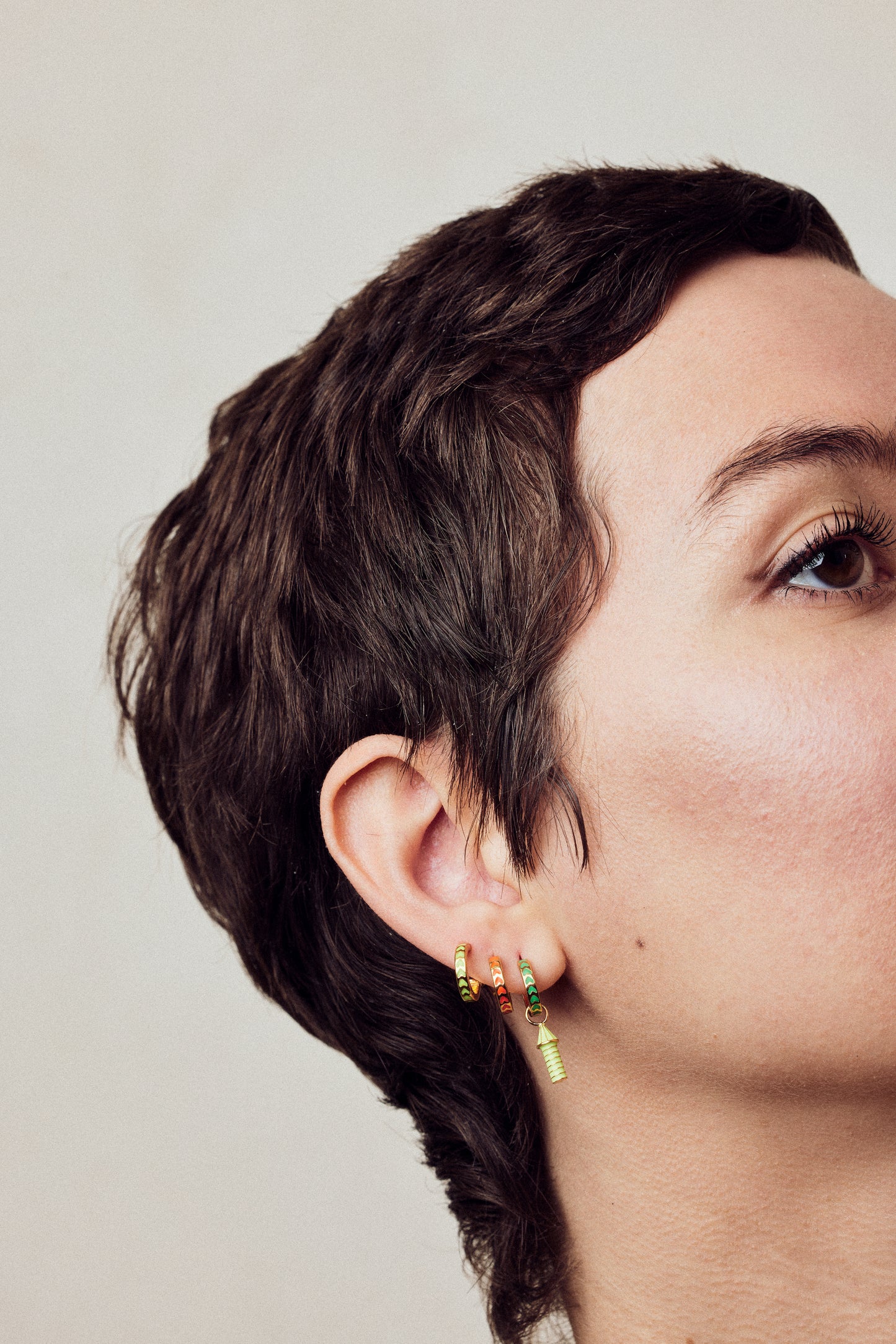 image of spark hoop enamel earrings stacked on ear with rocket enamel earrings on model with short brown hair