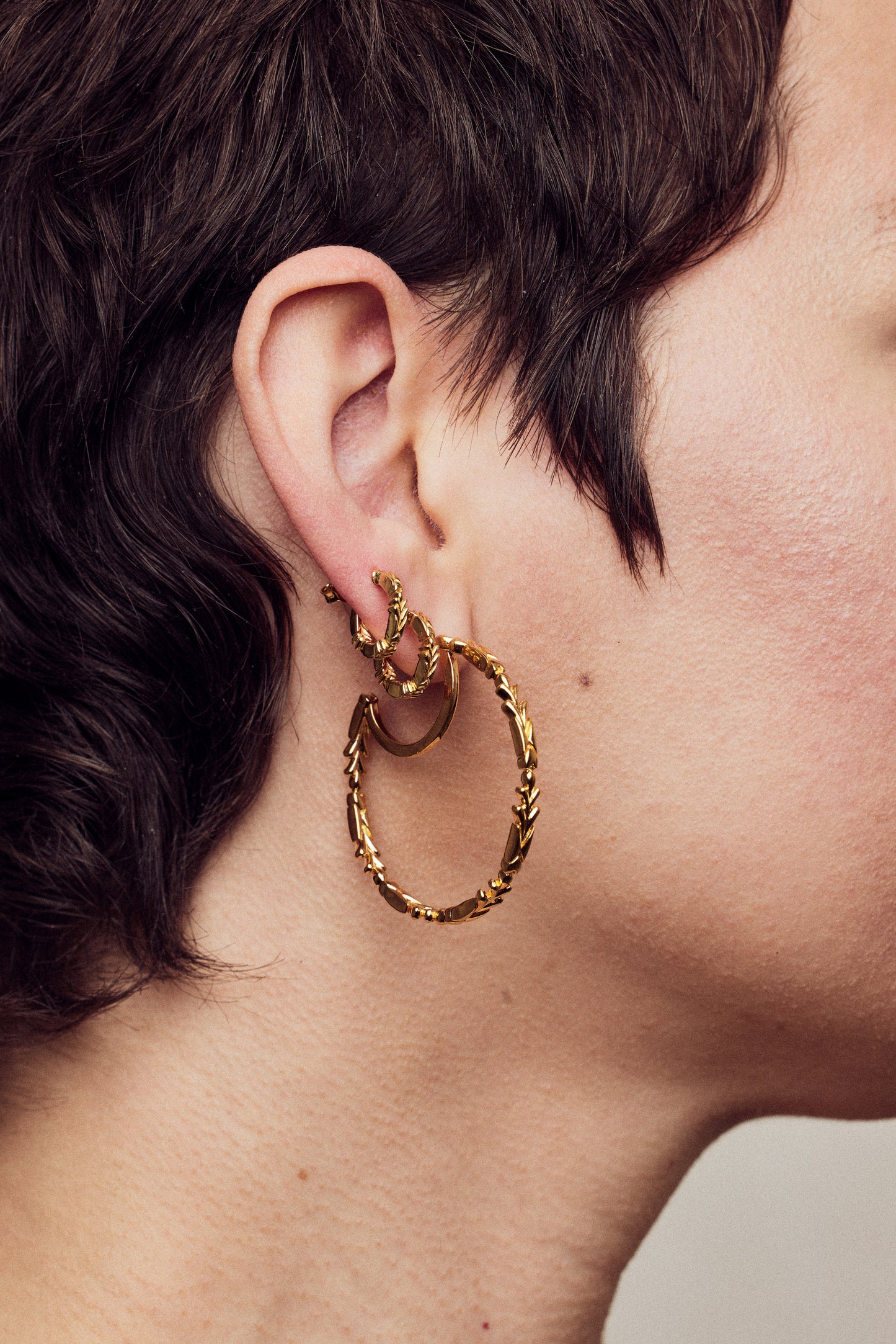 image of firework gold hoop earrings stacked on model with short brown hair