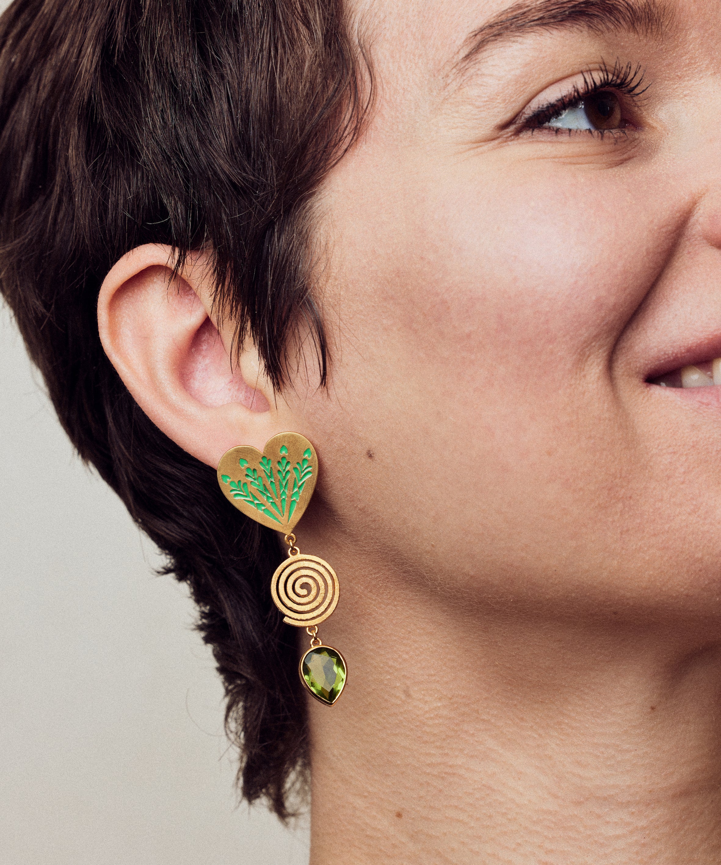 image of large firework heart earrings in green and gold on model close up smiling