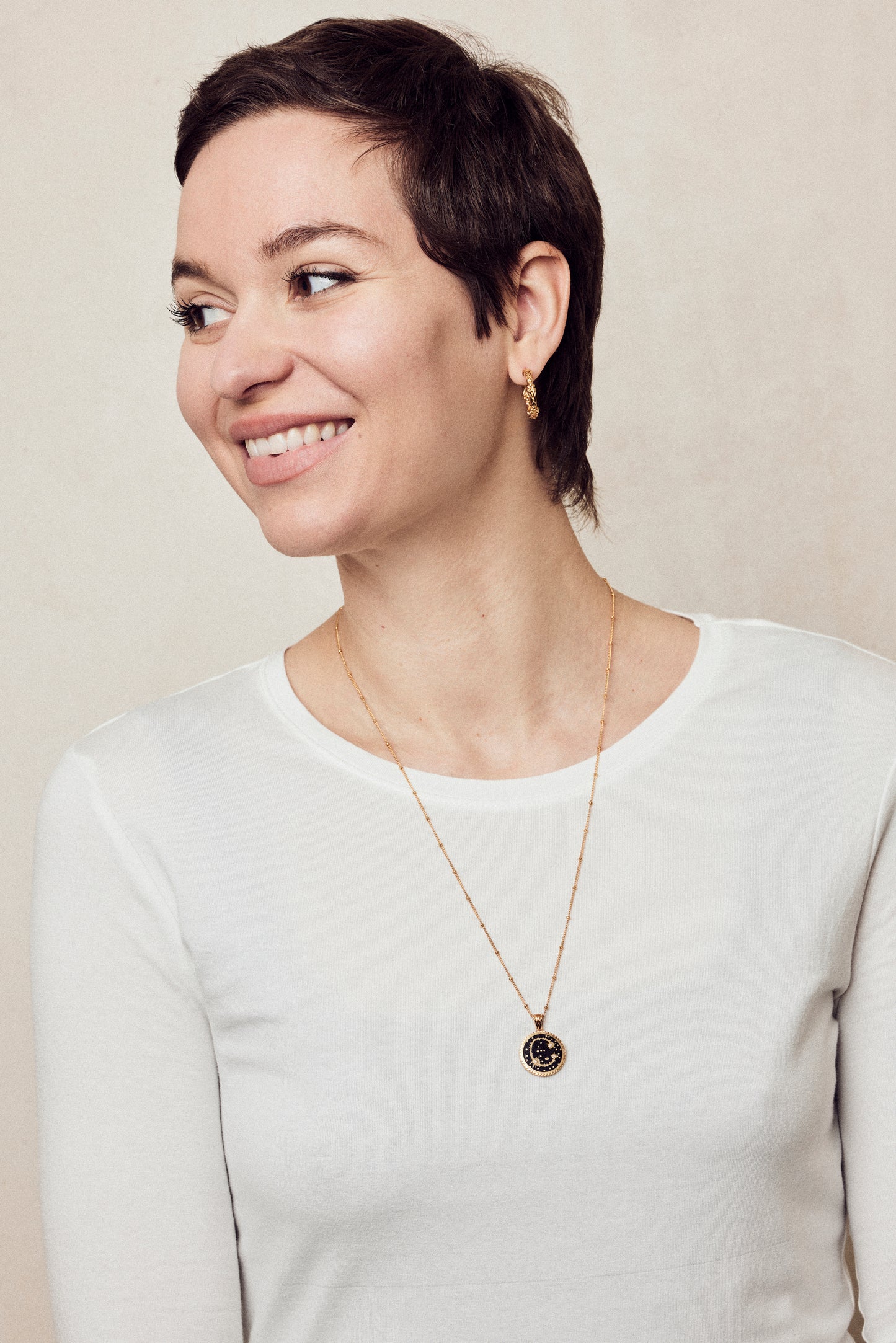image of sparkler diamond initial necklace, letter C on long chain, on model in white long-sleeved top with short brown hair smiling