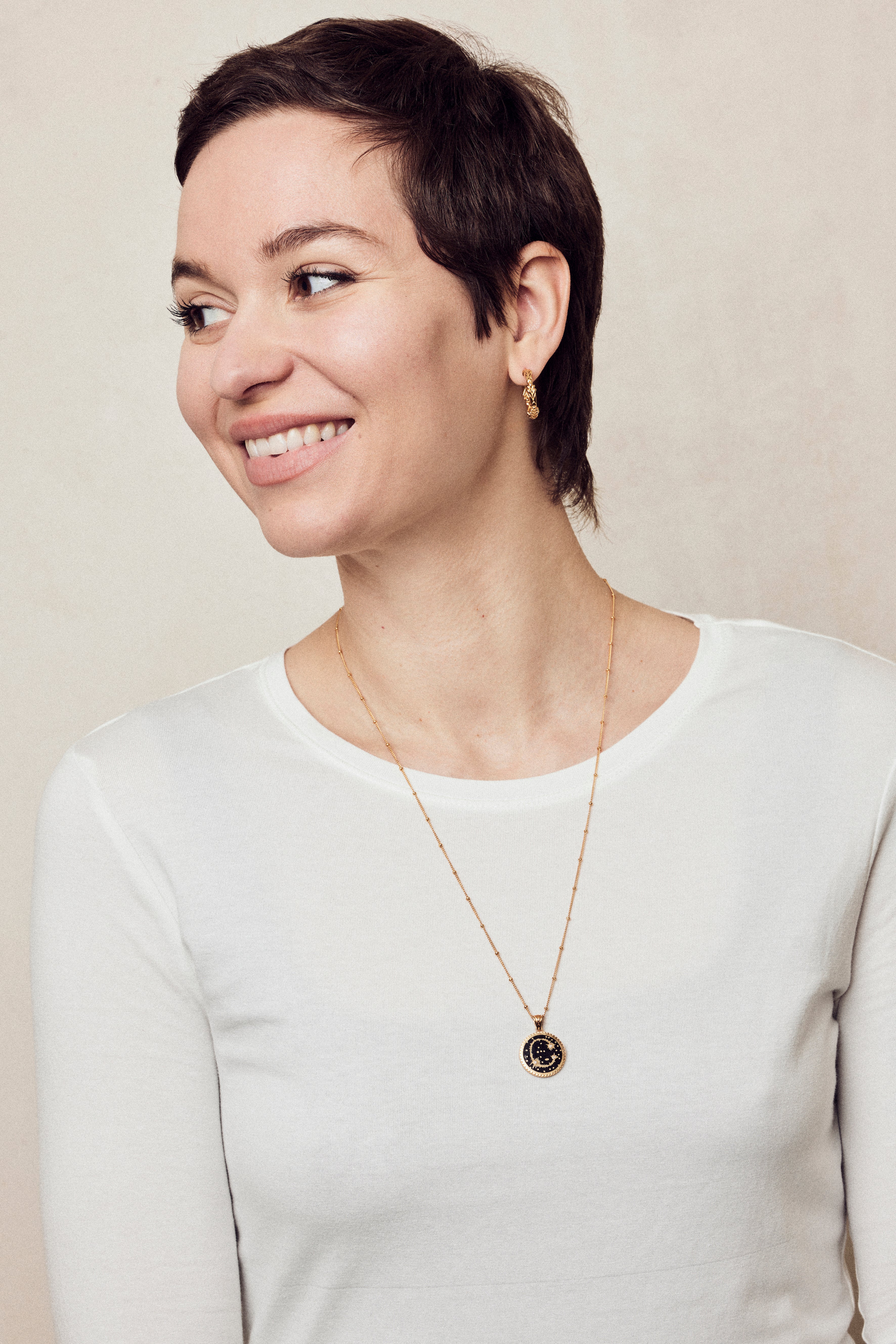  image of sparkler diamond initial necklace, letter C on long chain, on model in white long-sleeved top with short brown hair smiling