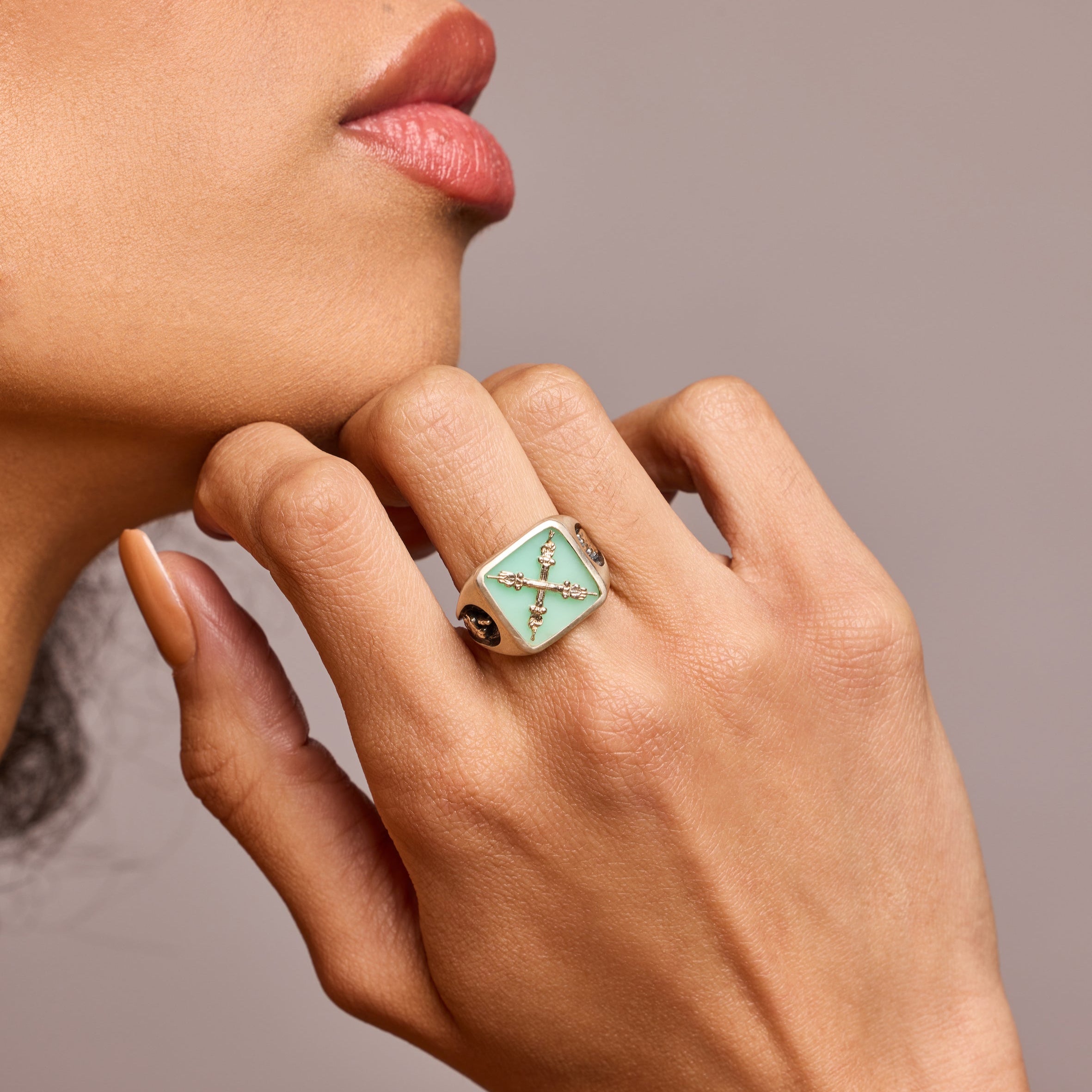 A signet ring in silver with semi-precious stone chrysoprase with a motif of one hand bearing the middle finger and the other their fingers crossed. On a model with her had up against her chin