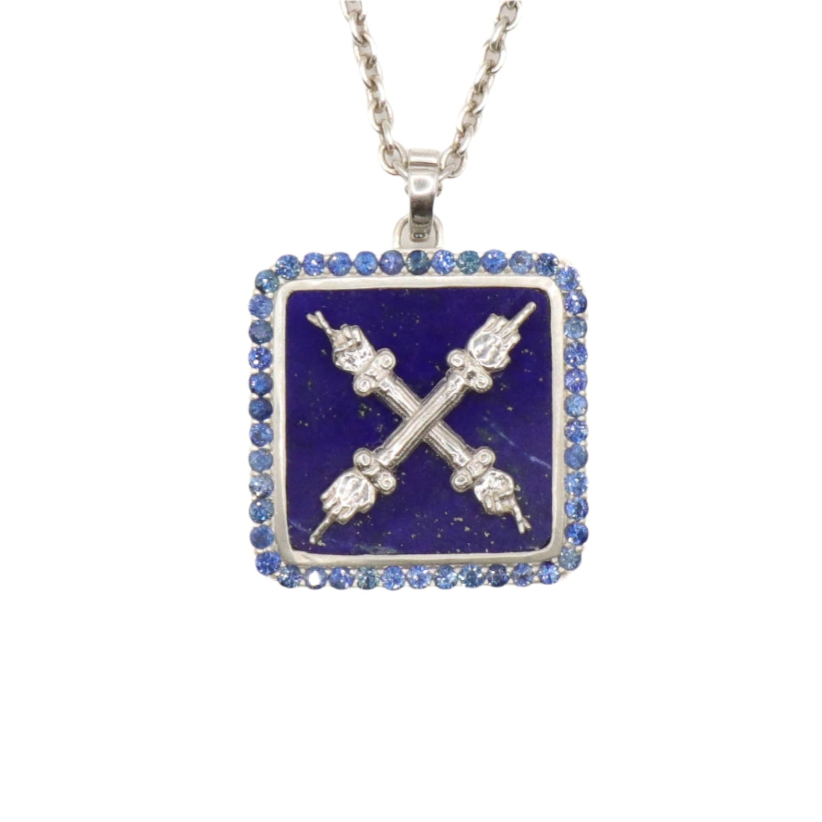 A necklace with a square pendant featuring a silver emblem on a lapis lazuli background, surrounded by blue sapphires, and a chain attached to the top.