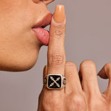 Signet ring in black onyx showing crest design with two hands on model with her finger to her lips making 'be quiet' sign