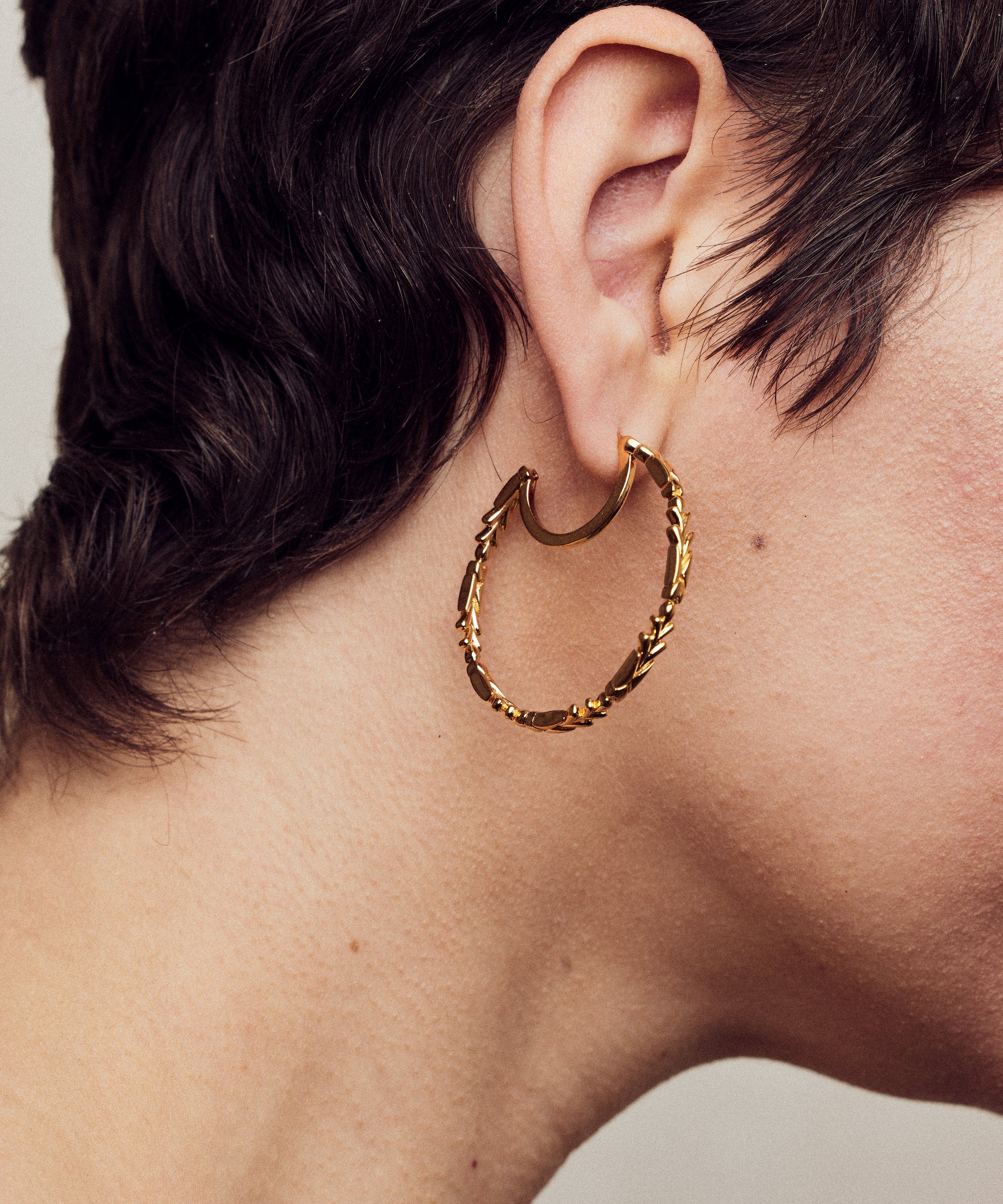 image of large firework gold hoop earrings close up on ear of model with short brown hair