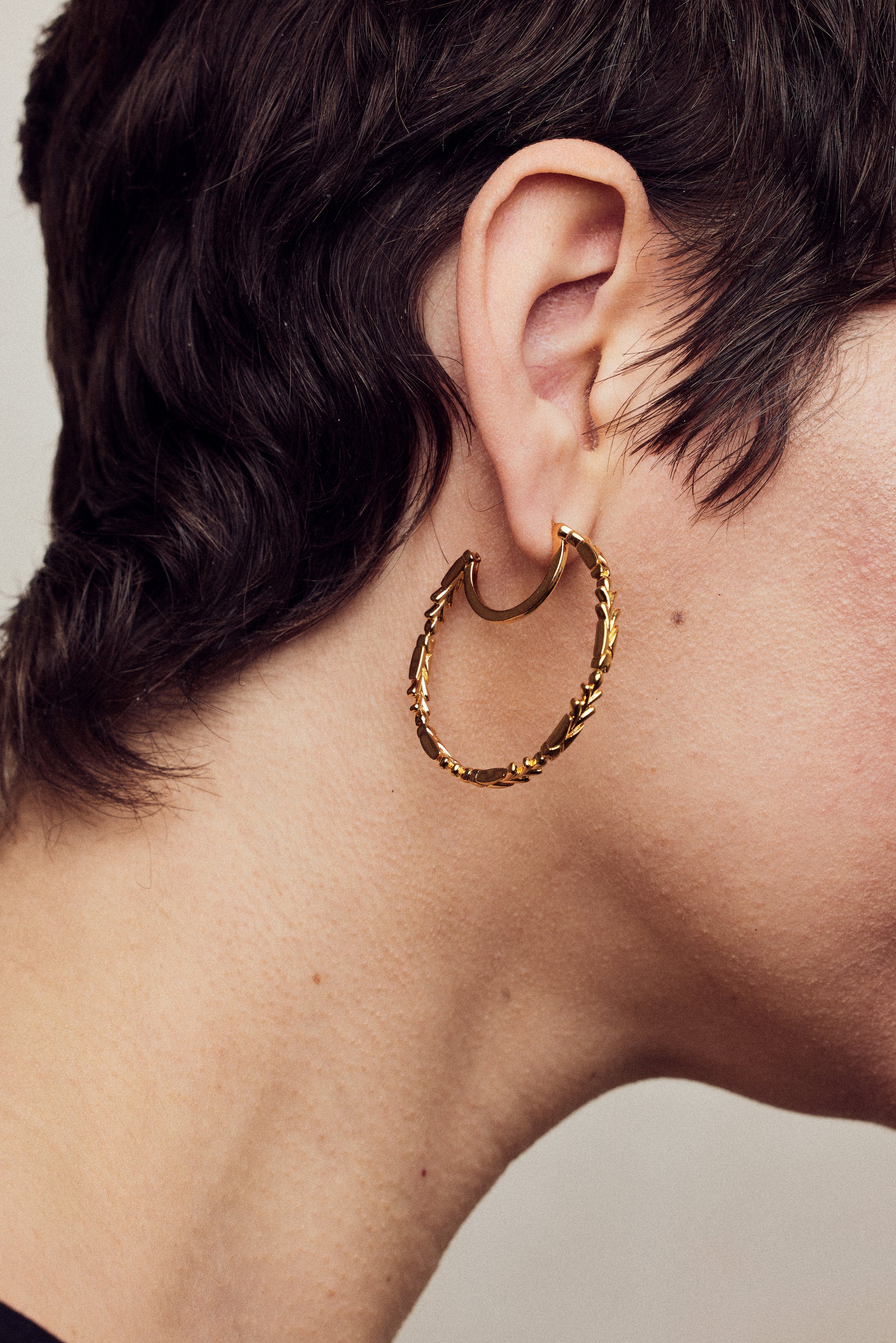 image of large firework gold hoop earrings close up on ear of model with short brown hair