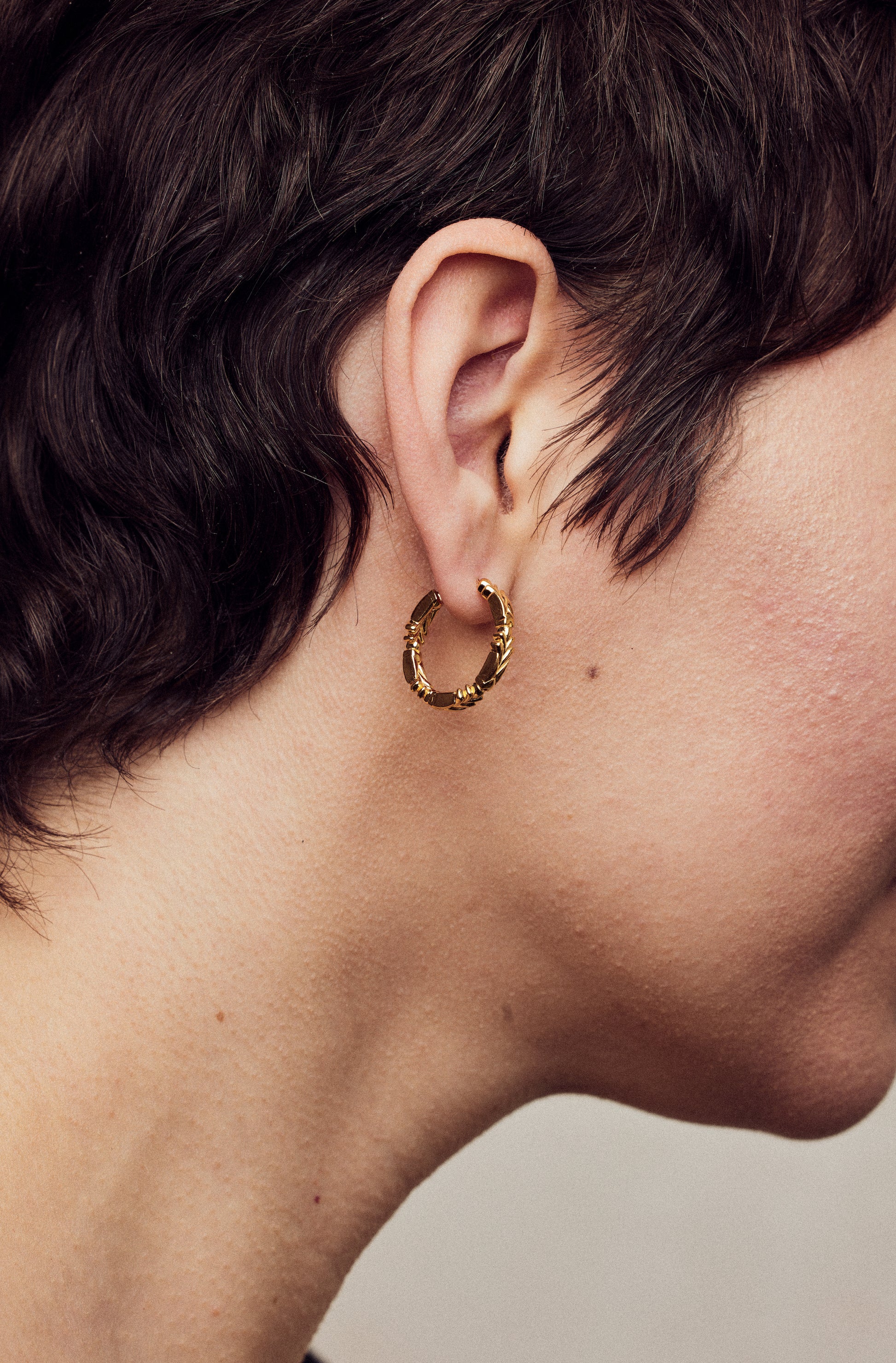 image of medium firework gold hoop earrings close up on ear on model with short brown hair