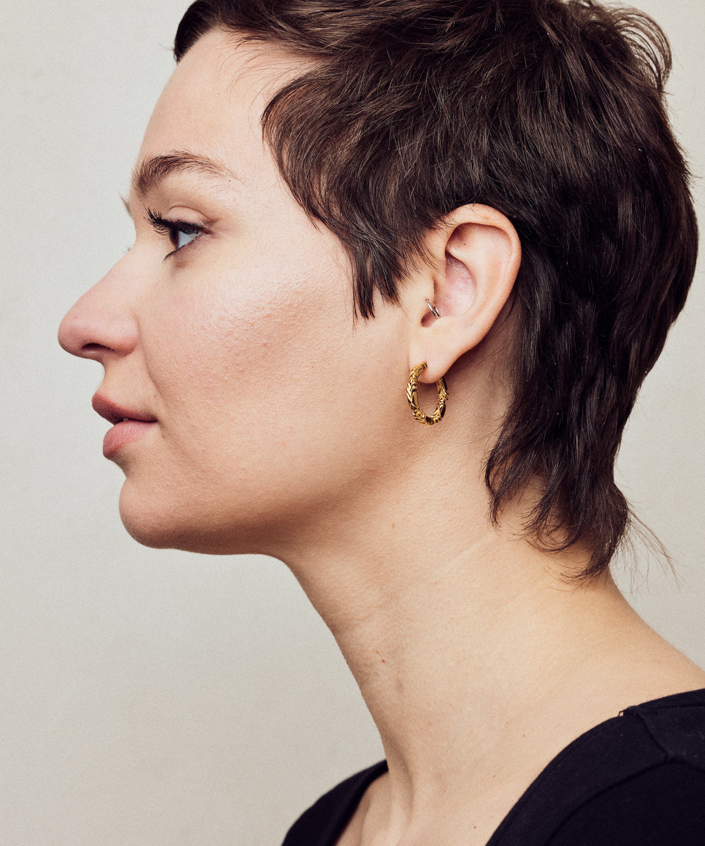 image of medium firework gold hoop earrings on model with short brown hair, headshot facing left