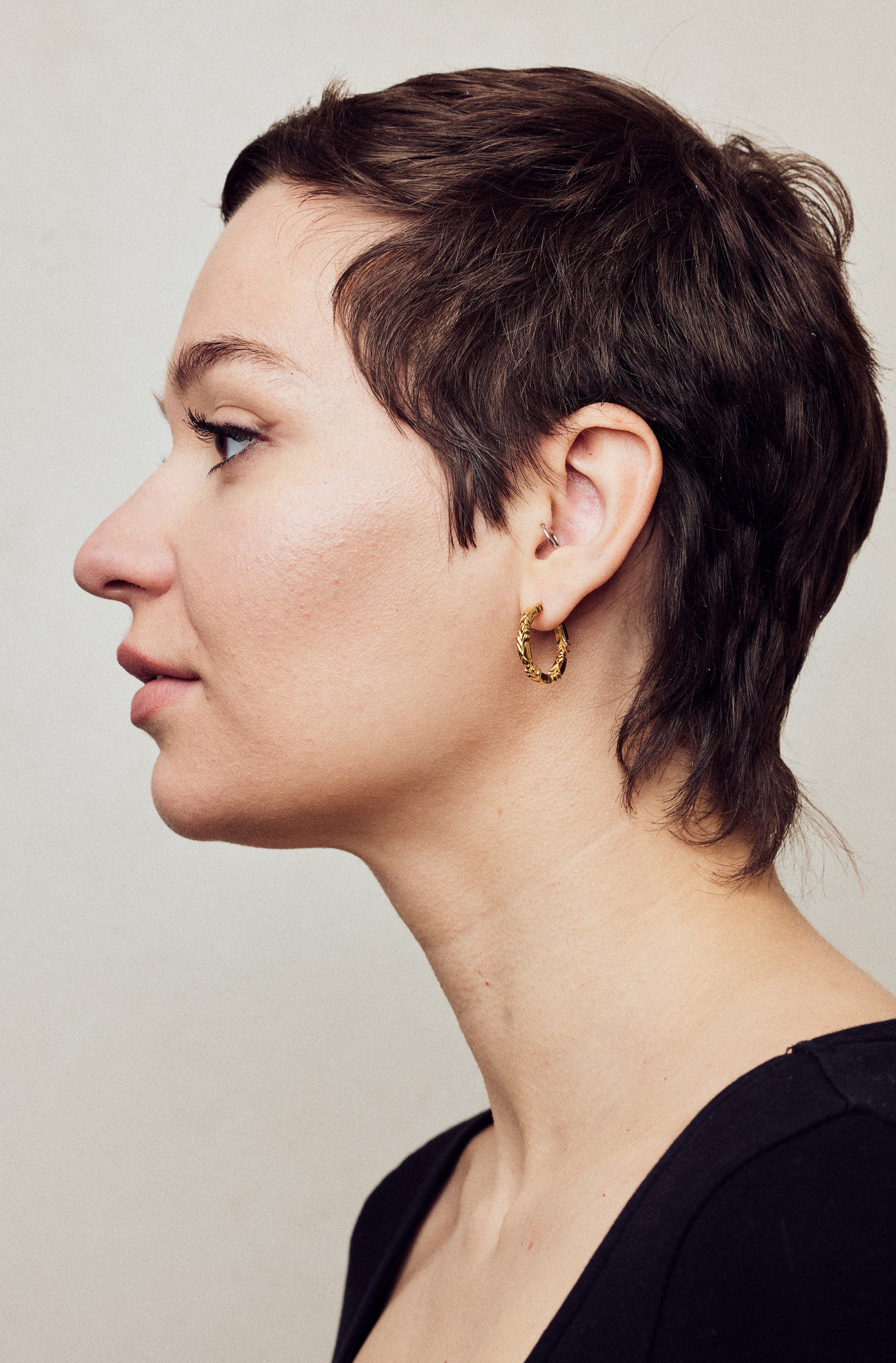 image of medium firework gold hoop earrings on model with short brown hair, headshot facing left