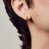 image of firework gold mini hoops close up on ear on model with short brown hair