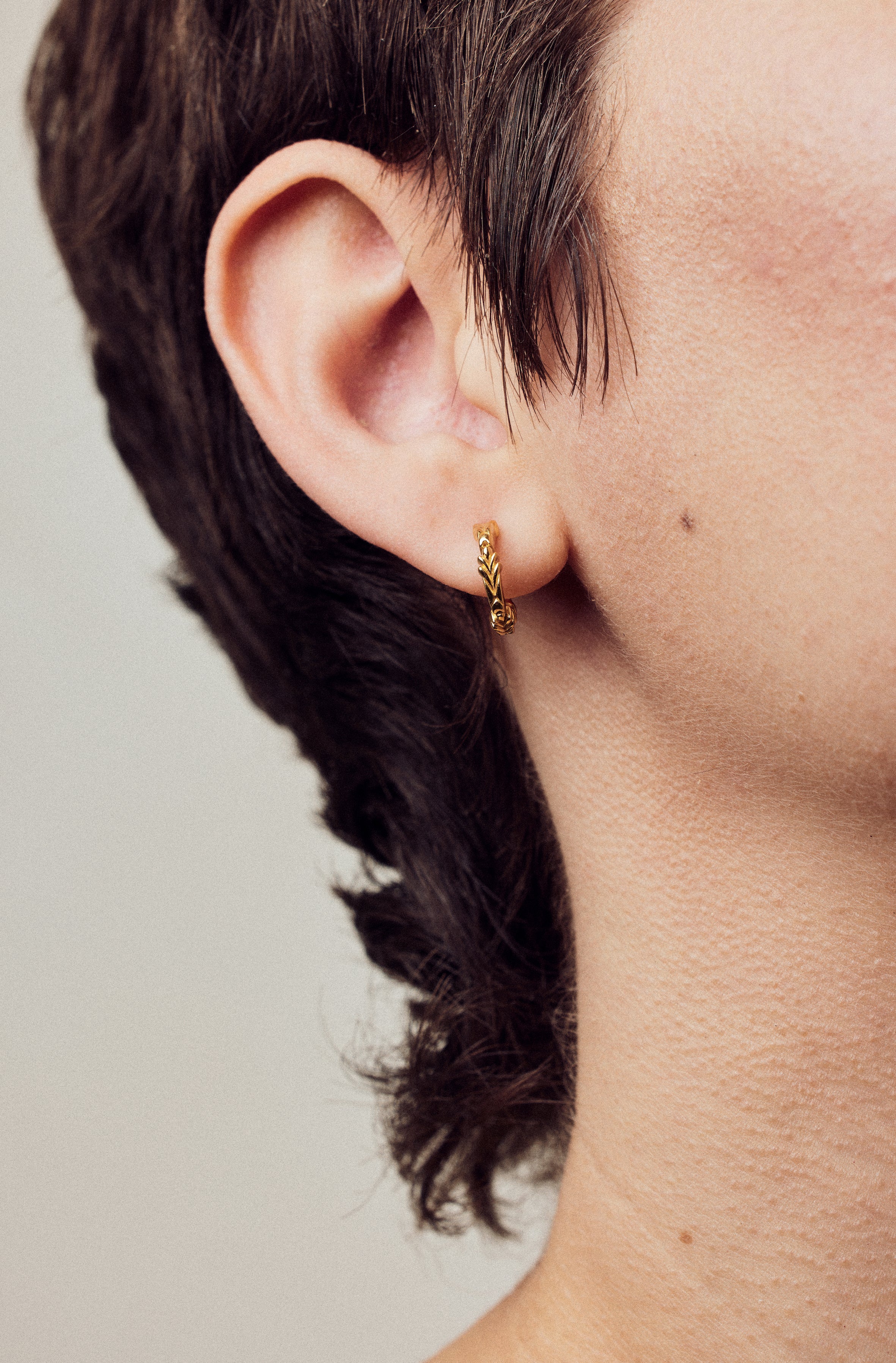 image of firework gold mini hoops close up on ear on model with short brown hair