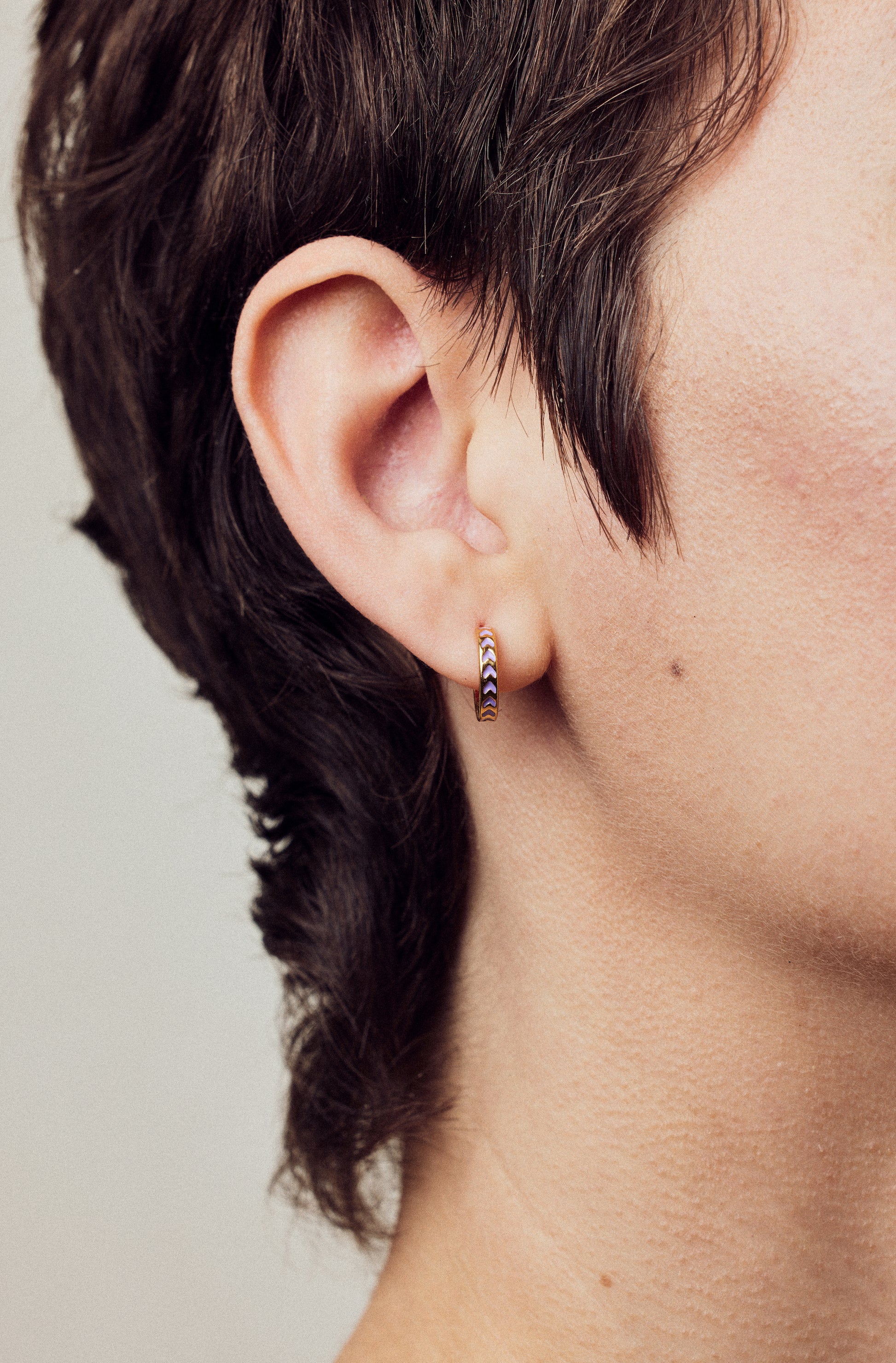 image of spark hoop enamel earrings in purple and gold, close up on ear of model with white skin and short brown hair