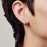 image of spark hoop enamel earrings in purple and gold shown close-up on ear of model with white skin and short brown hair
