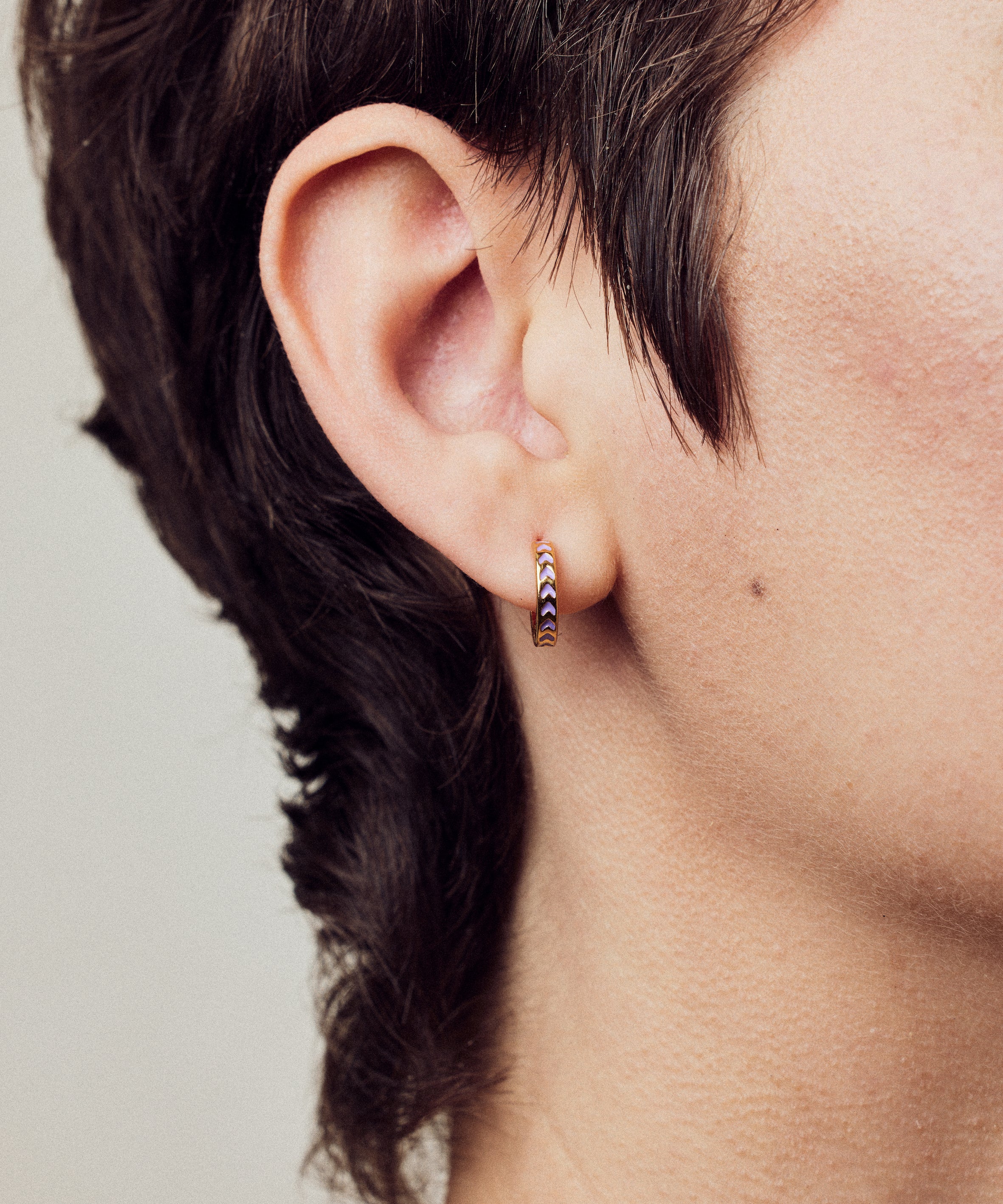 image of spark hoop enamel earrings in purple and gold shown close-up on ear of model with white skin and short brown hair