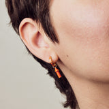 image of rocket enamel earrings in orange and gold shown close-up of ear and eye on model with white skin and short brown hair