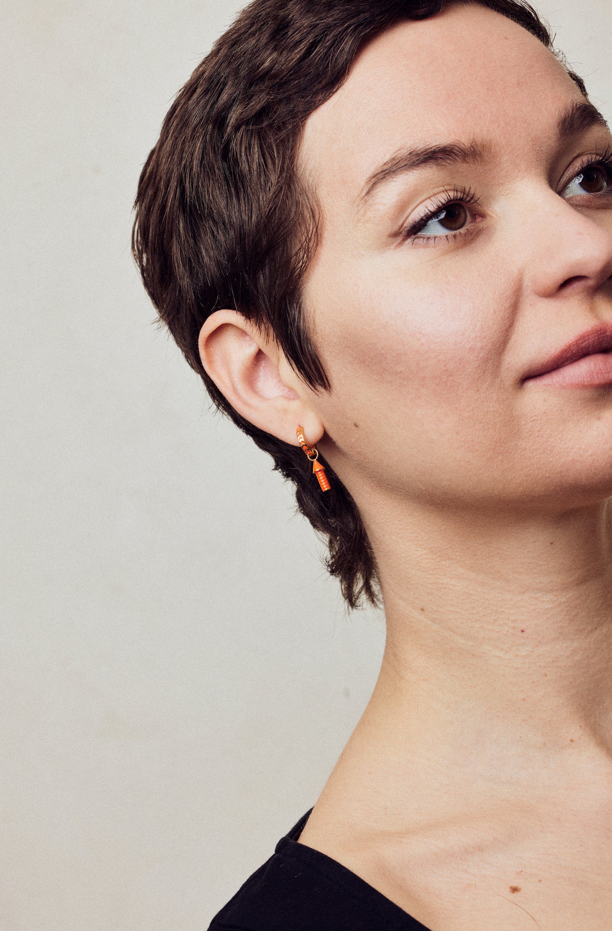 image of rocket enamel earrings in orange and gold shown on model with white skin and short brown hair