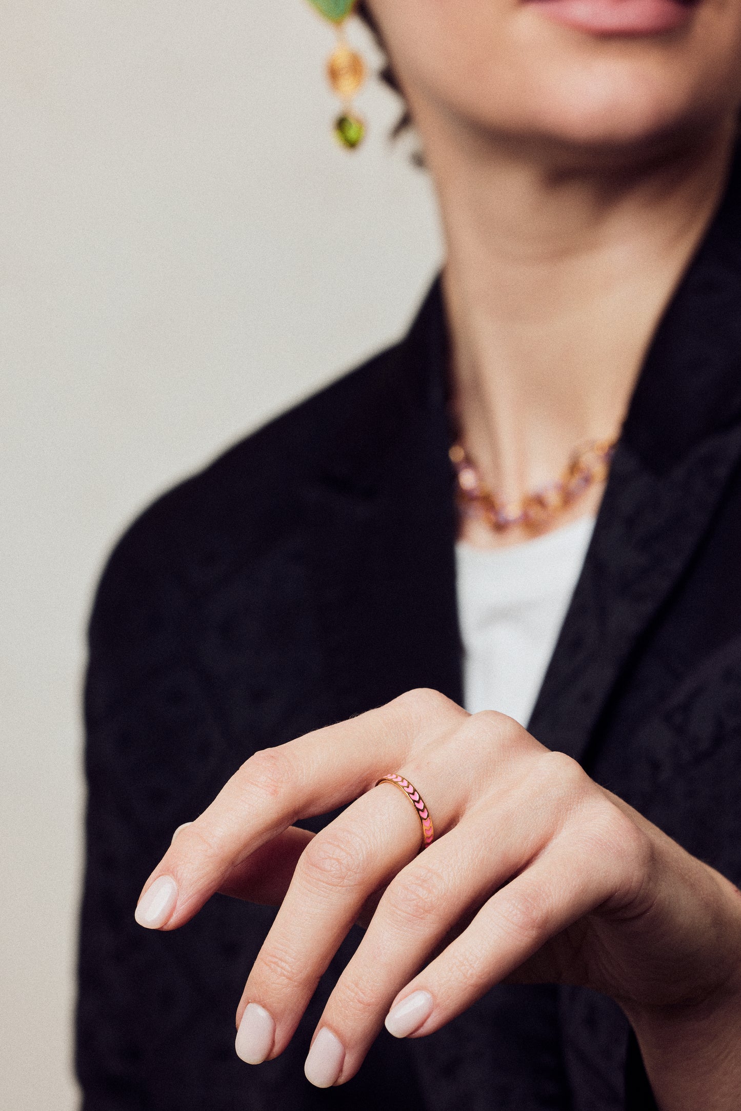 image of spark enamel ring in pink and gold on hand in forefront of image on model in black jacket