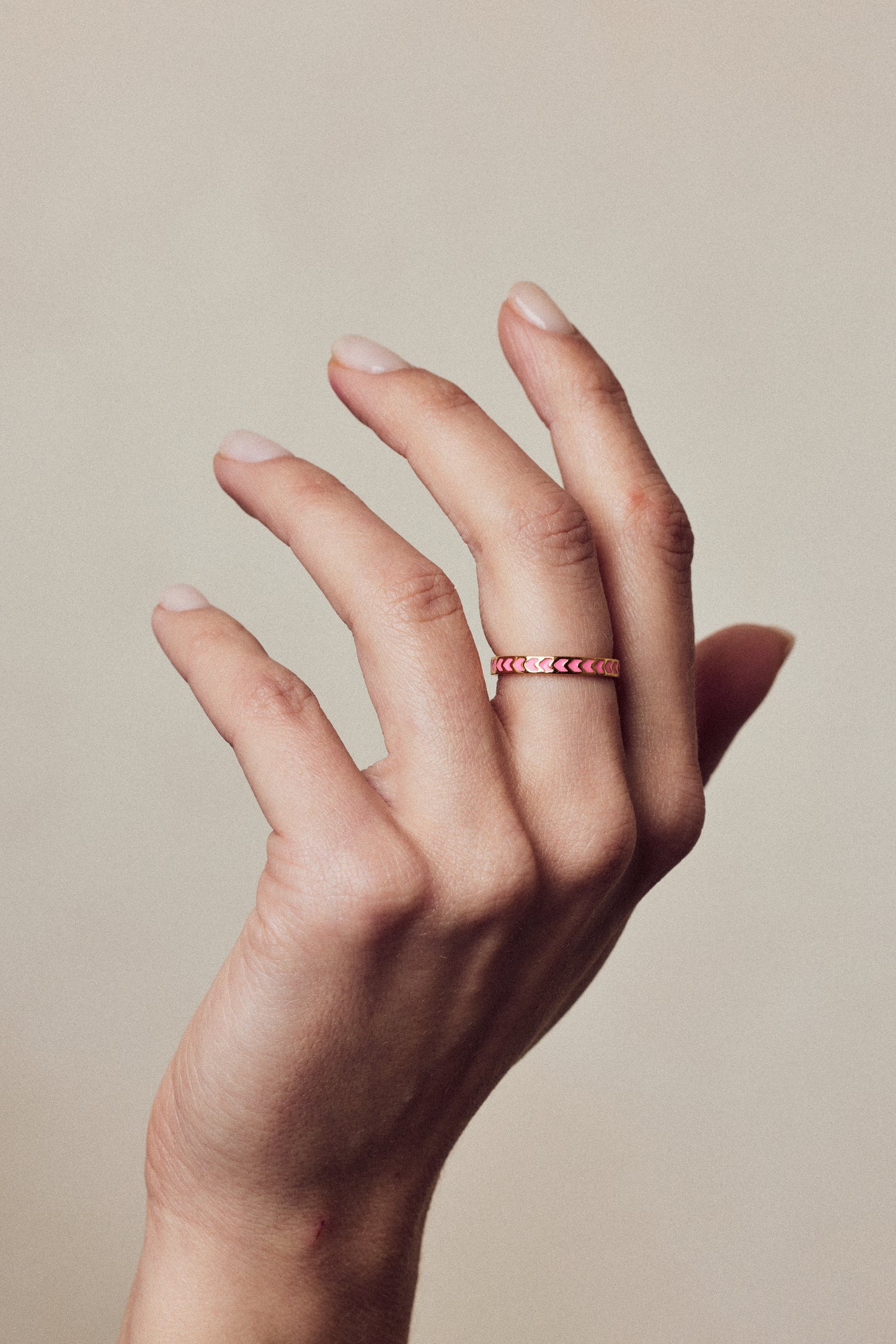 image of spark enamel ring in pink and gold on hand with fingers stretched upwards against beige background