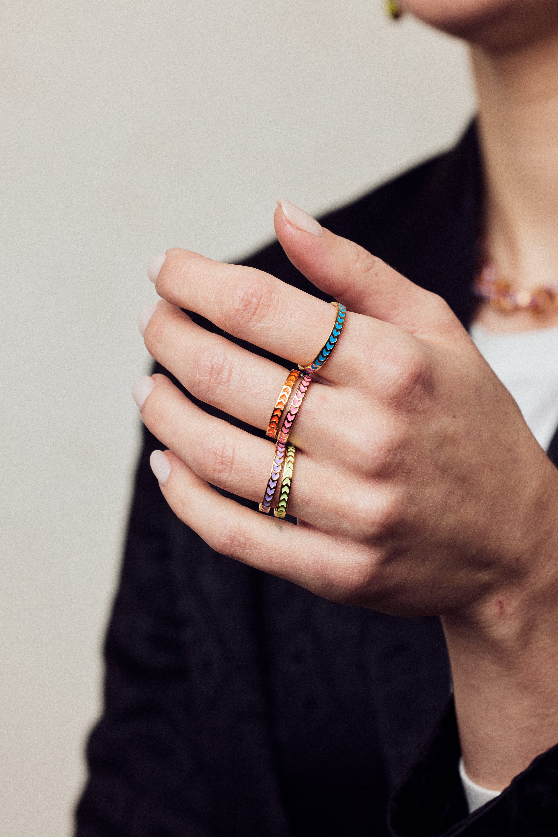 image of spark enamel rings in six colours of enamel and gold on hand in forefront of image on model in black jacket