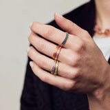 image of spark enamel rings in six colours of enamel and gold on hand in forefront of image on model in black jacket