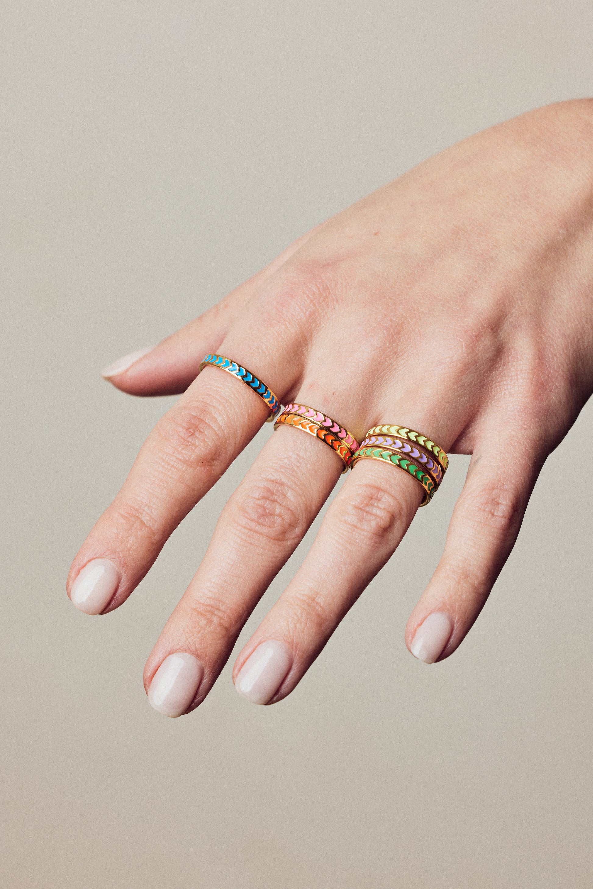 image of spark enamel rings in six colours of enamel and gold on hand with white skin against a beige wall