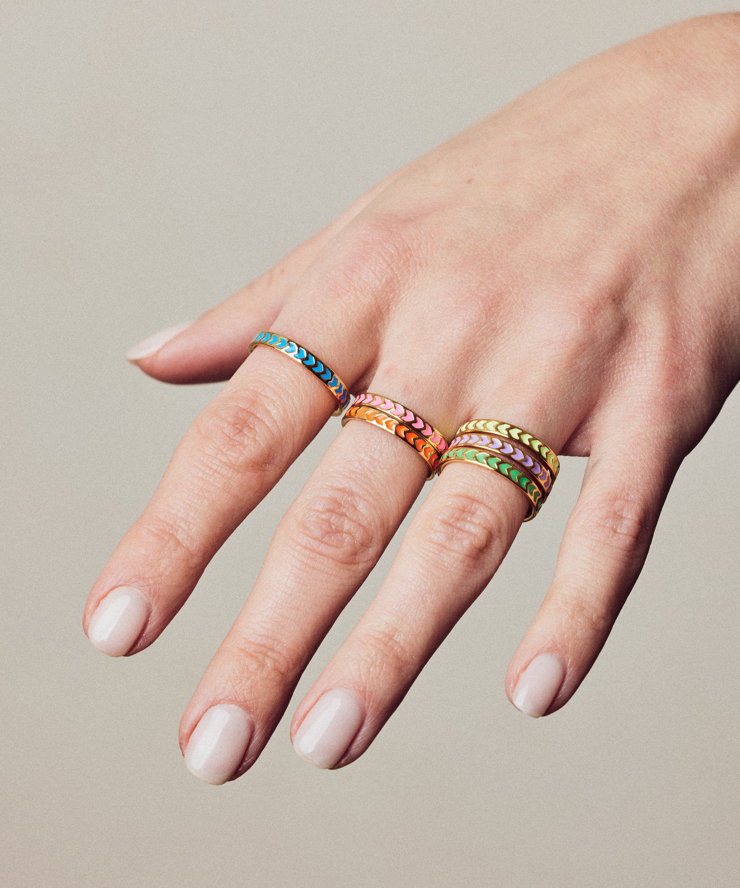 image of spark enamel rings in six colours of enamel and gold on hand with white skin against a beige wall