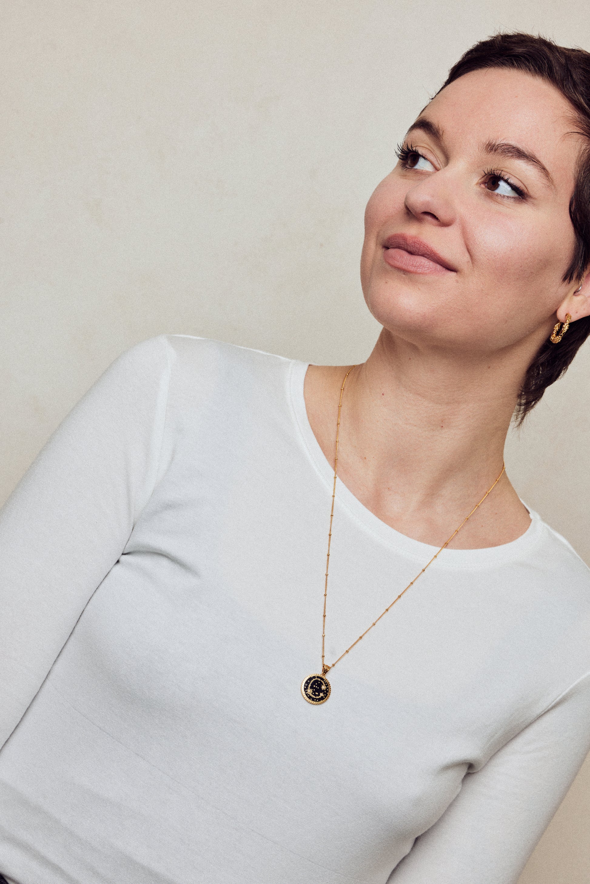 image of sparkler diamond initial necklace, letter C on long chain, on model in white top with short brown hair looking off to the left