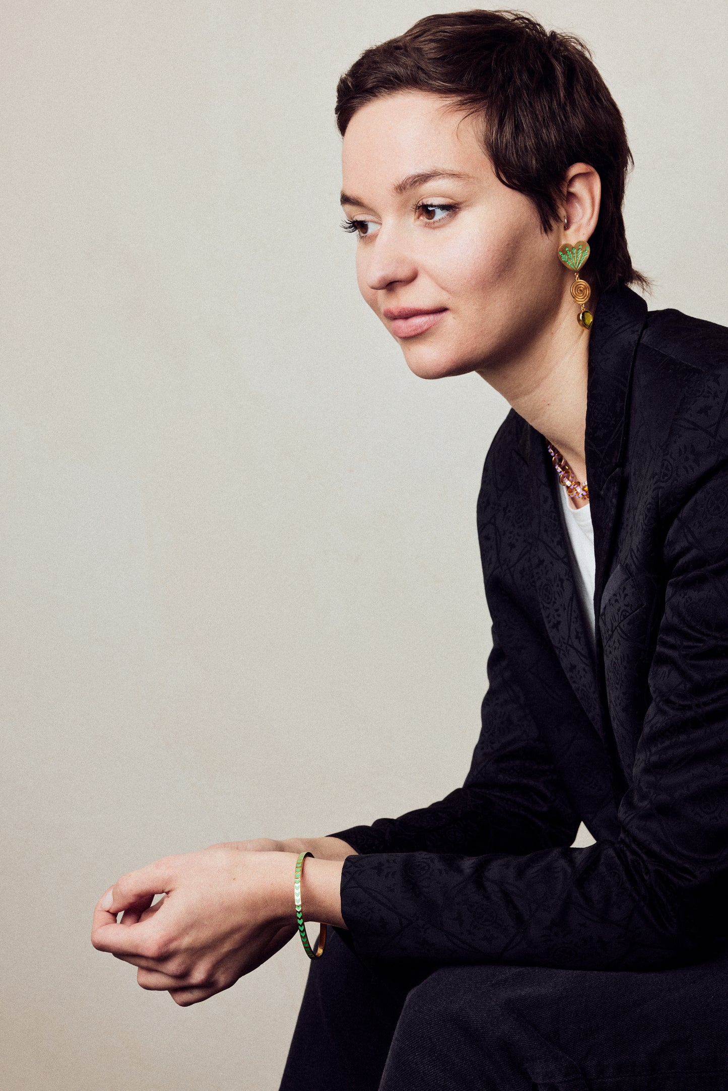 image of spark enamel bangle in green and gold on model seated wearing black jacket and black jeans