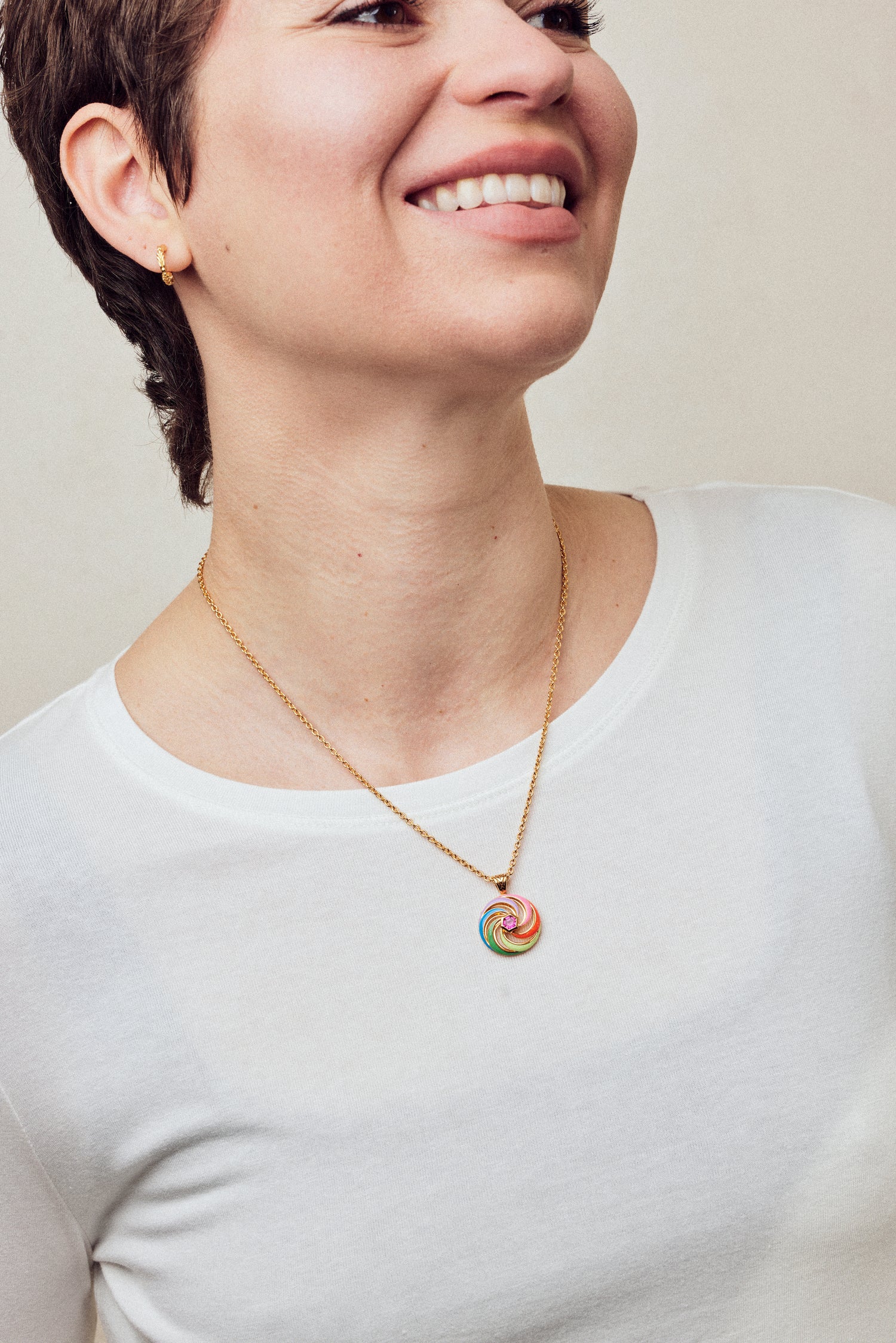 Image of enamel necklace with spinning disk on short chain on model in white top smiling