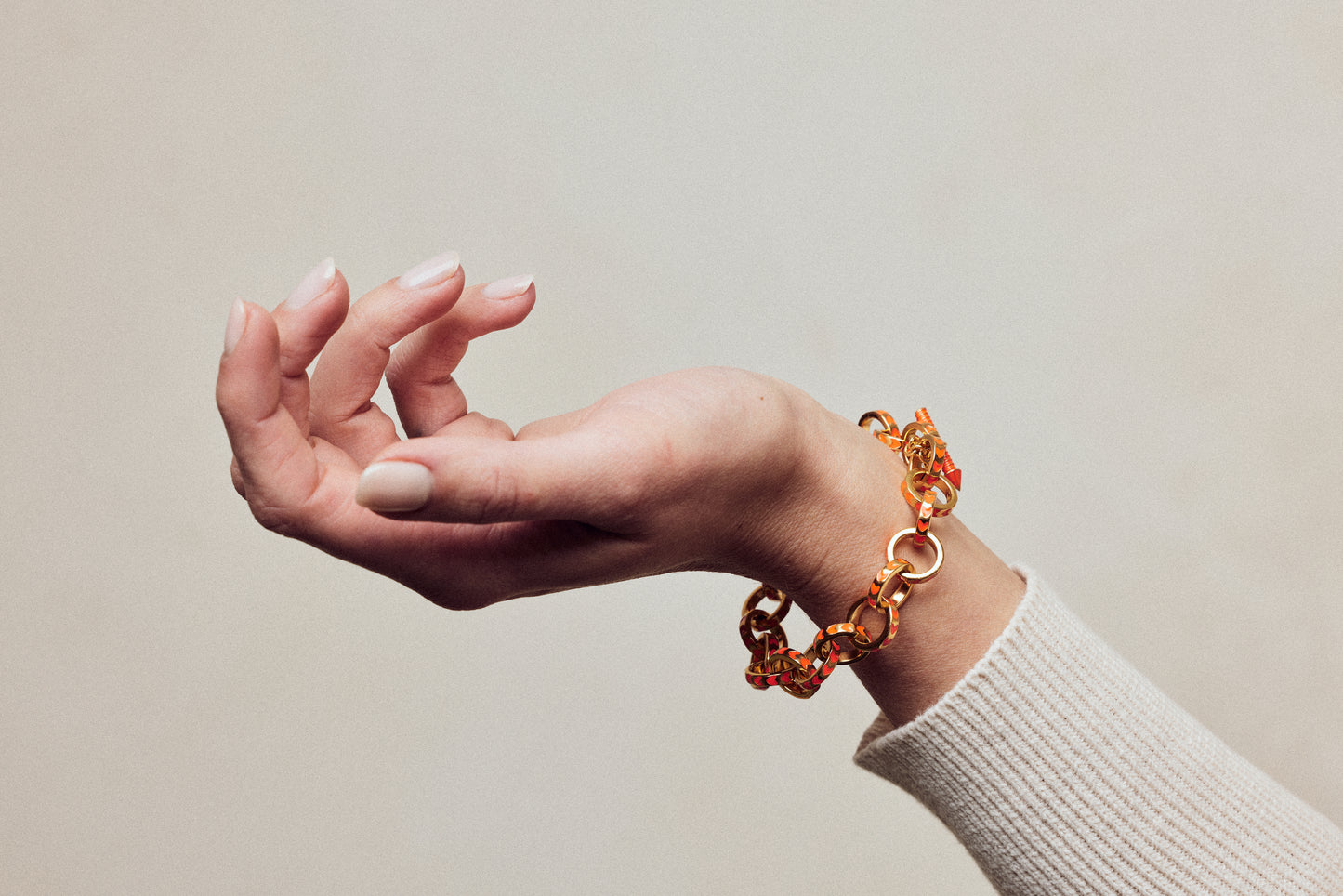 image of spark gold chain bracelet in orange and gold on wrist of woman with white skin wearing cream ribbed top showing hand upturned