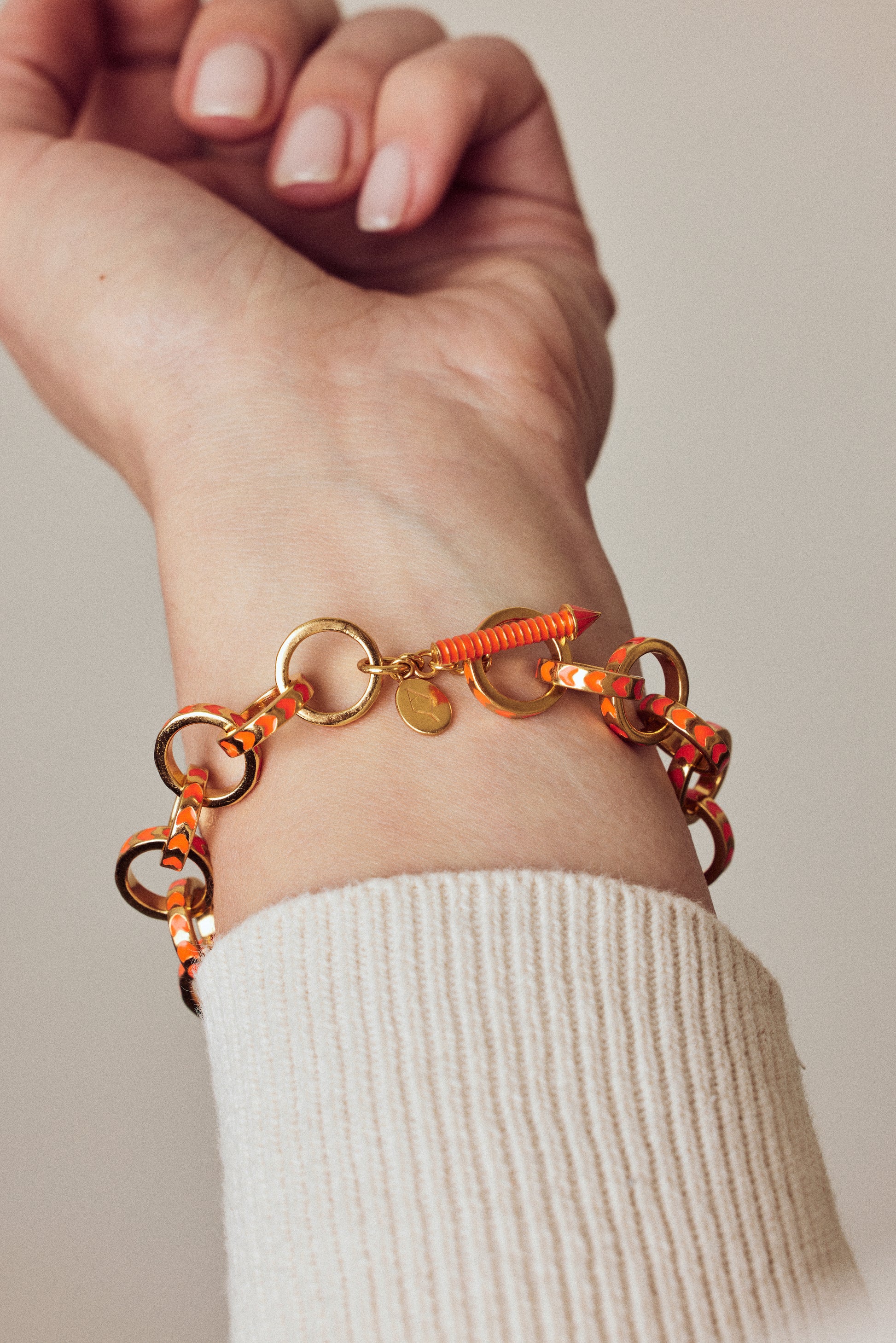 image of gold chain bracelet with orange enamel on wrist of model with hand outstretched and fingers curled