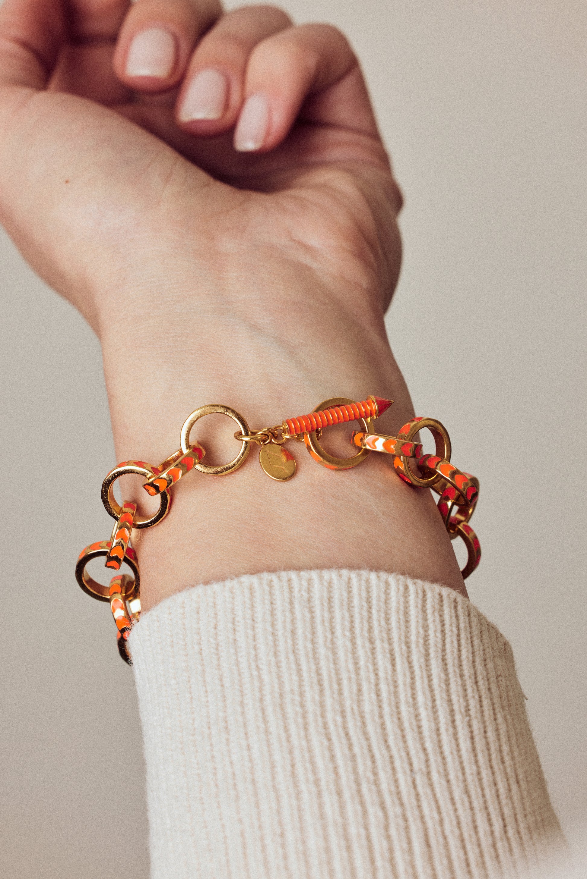 image of gold chain bracelet in orange of gold on wrist with arm outstretched in cream ribbed top