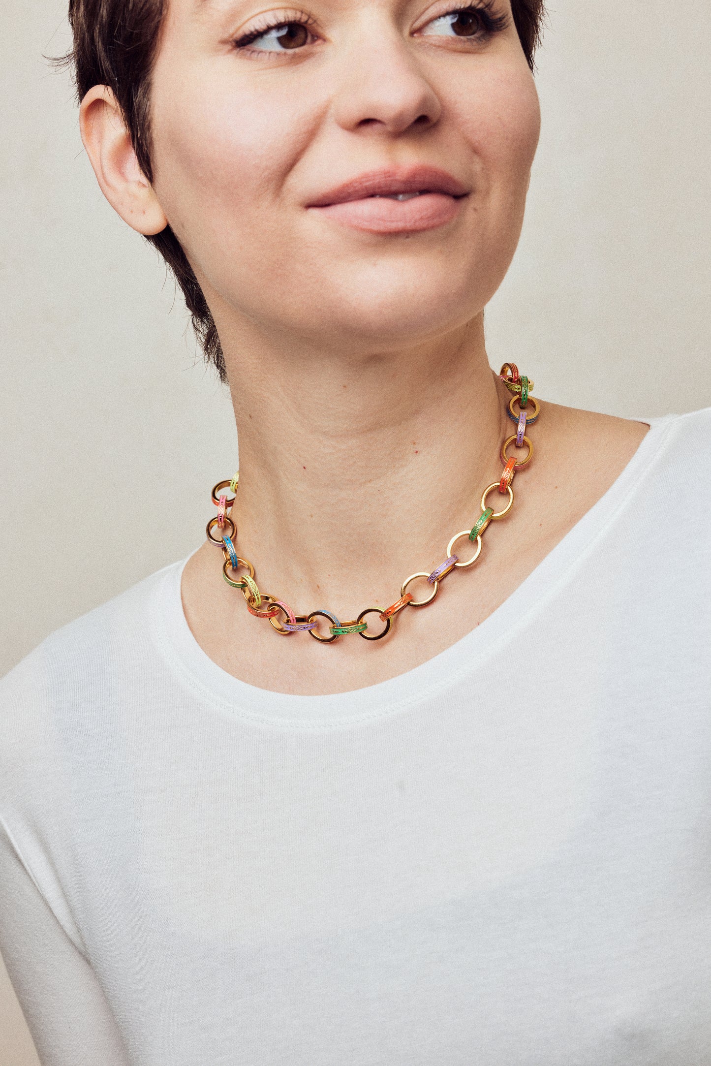 image of firework gold chain necklace with multi-coloured enamel on model in white top smiling