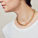 image of firework gold chain necklace with multi-coloured enamel on model facing left in white top