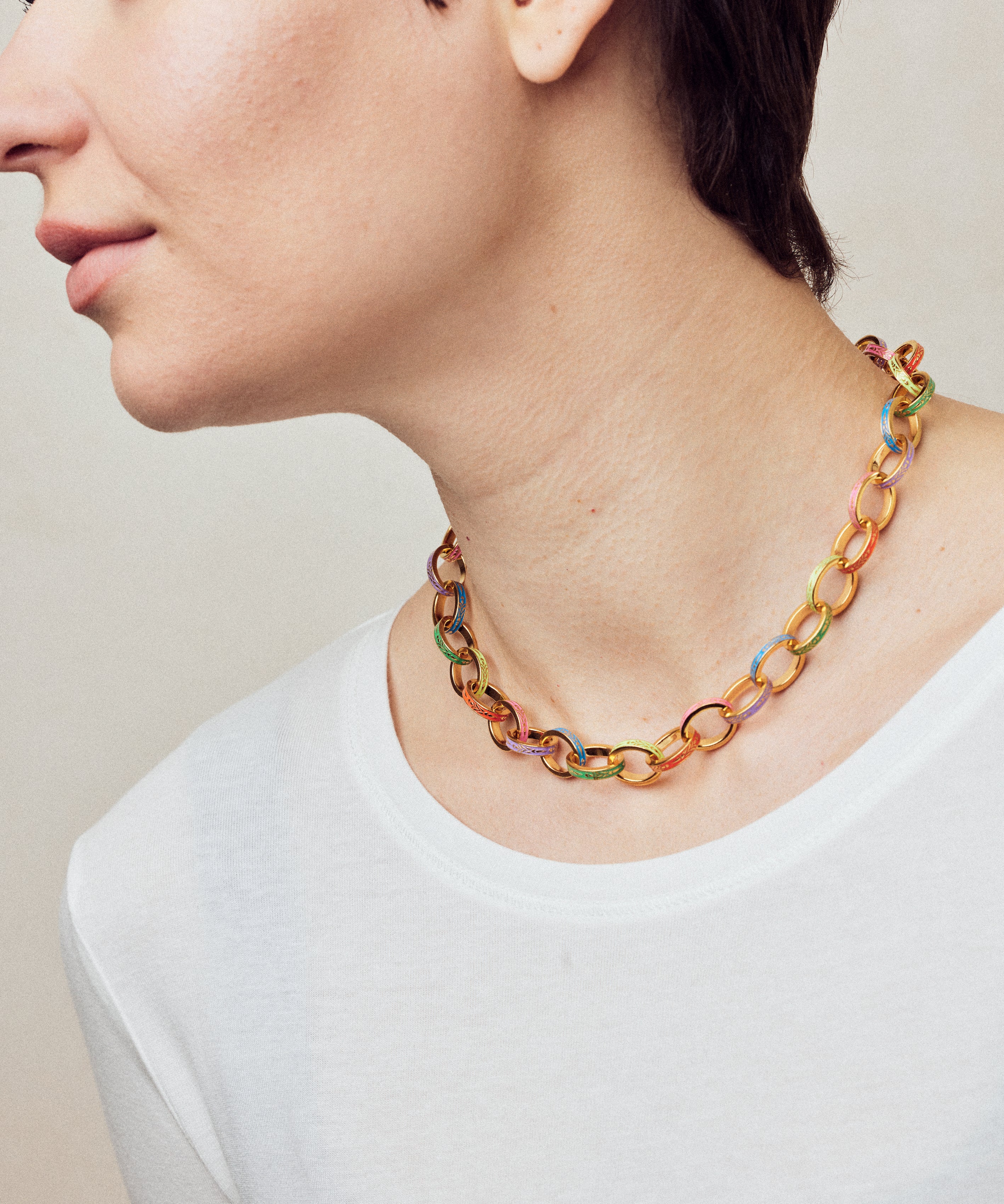 image of firework gold chain necklace with multi-coloured enamel on model facing left in white top