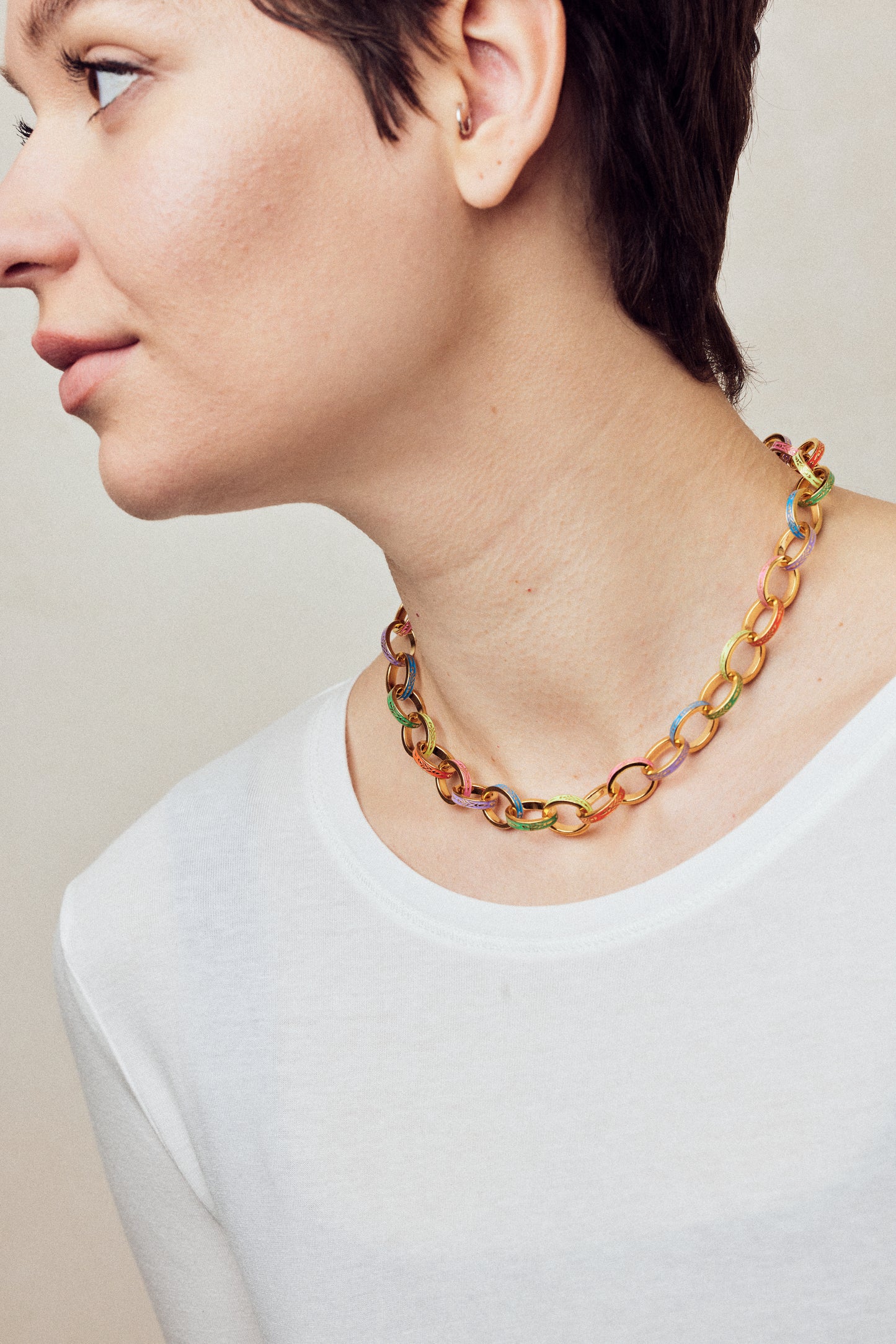 image of firework gold chain necklace with multi-coloured enamel on model facing left in white top