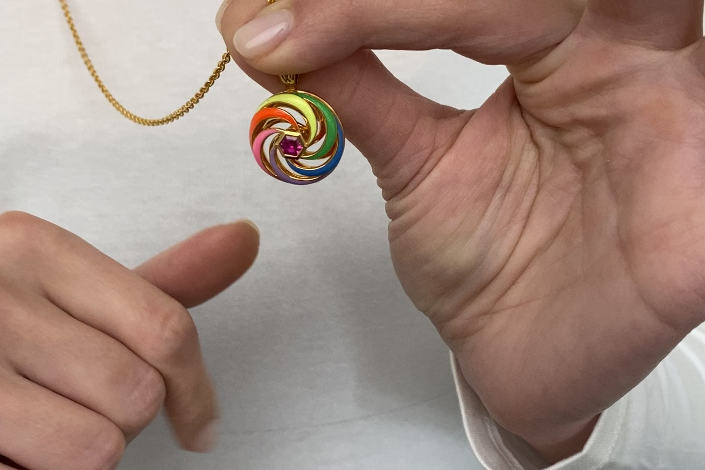video of spinning disk enamel necklace in multi-colour enamel with close up on hands of model spinning it 
